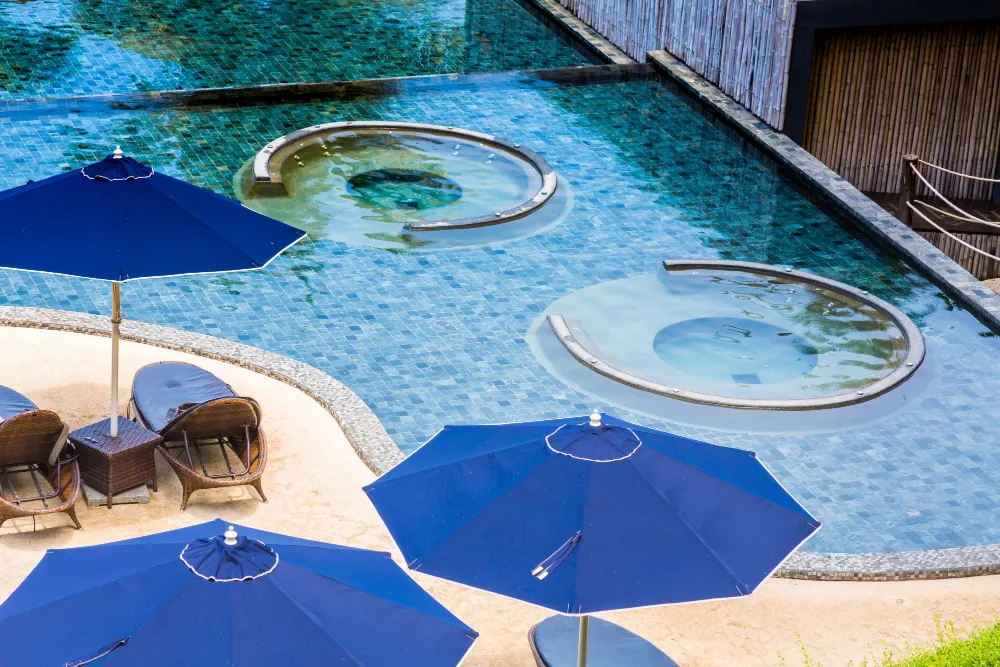 Resort-style swimming pool with circular spa areas and blue umbrellas along the poolside.