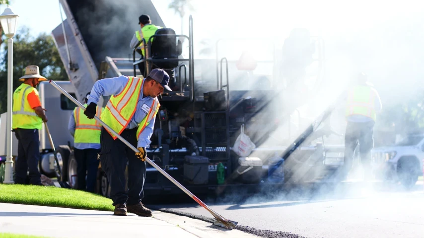 Asphalt dumptruck refilling paving machine while raker perfects edge of overlay