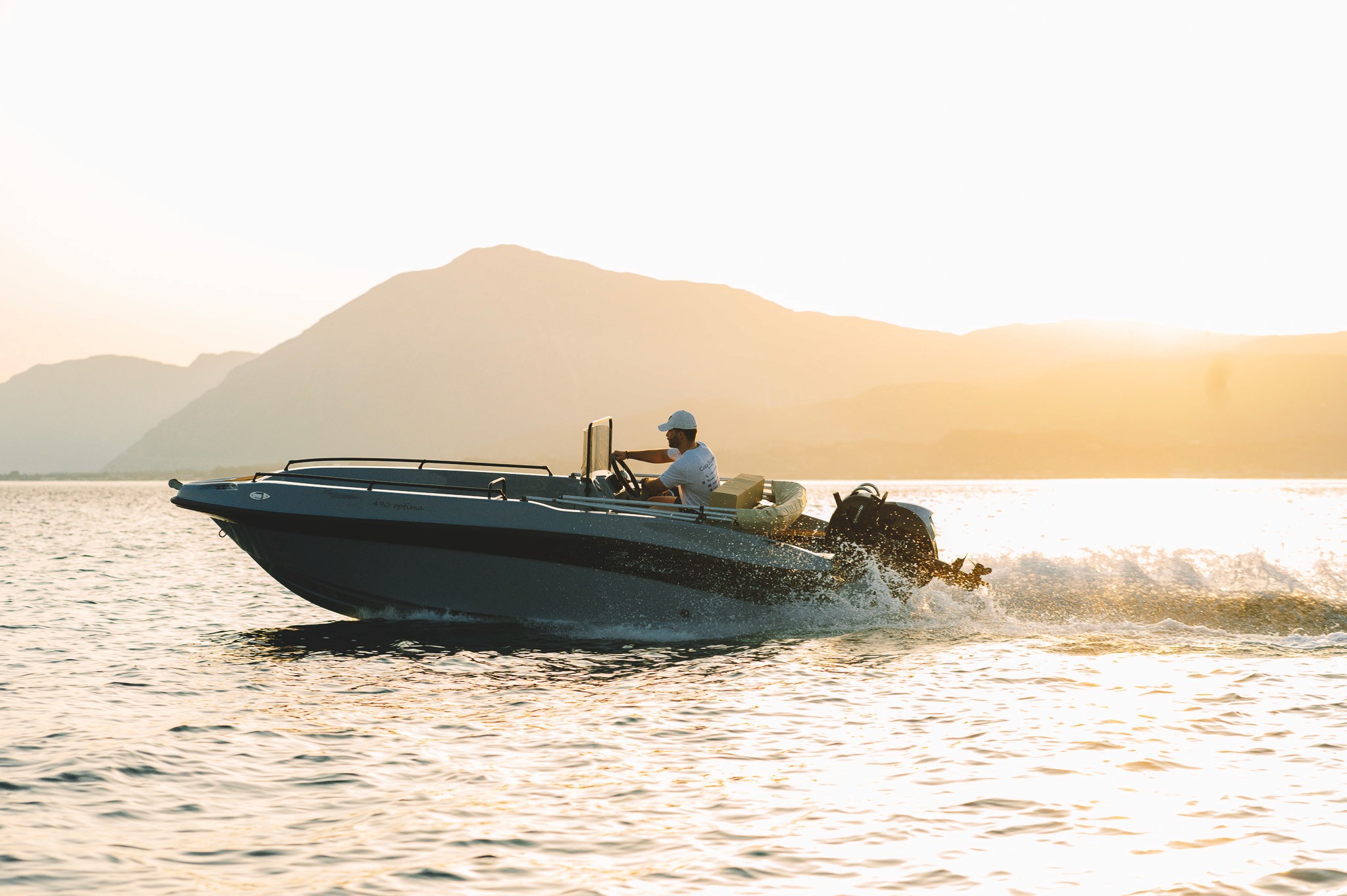 Sleek speedboat with captain cruising at sunset, creating spray wake against golden sky and mountainous Greek coastline.