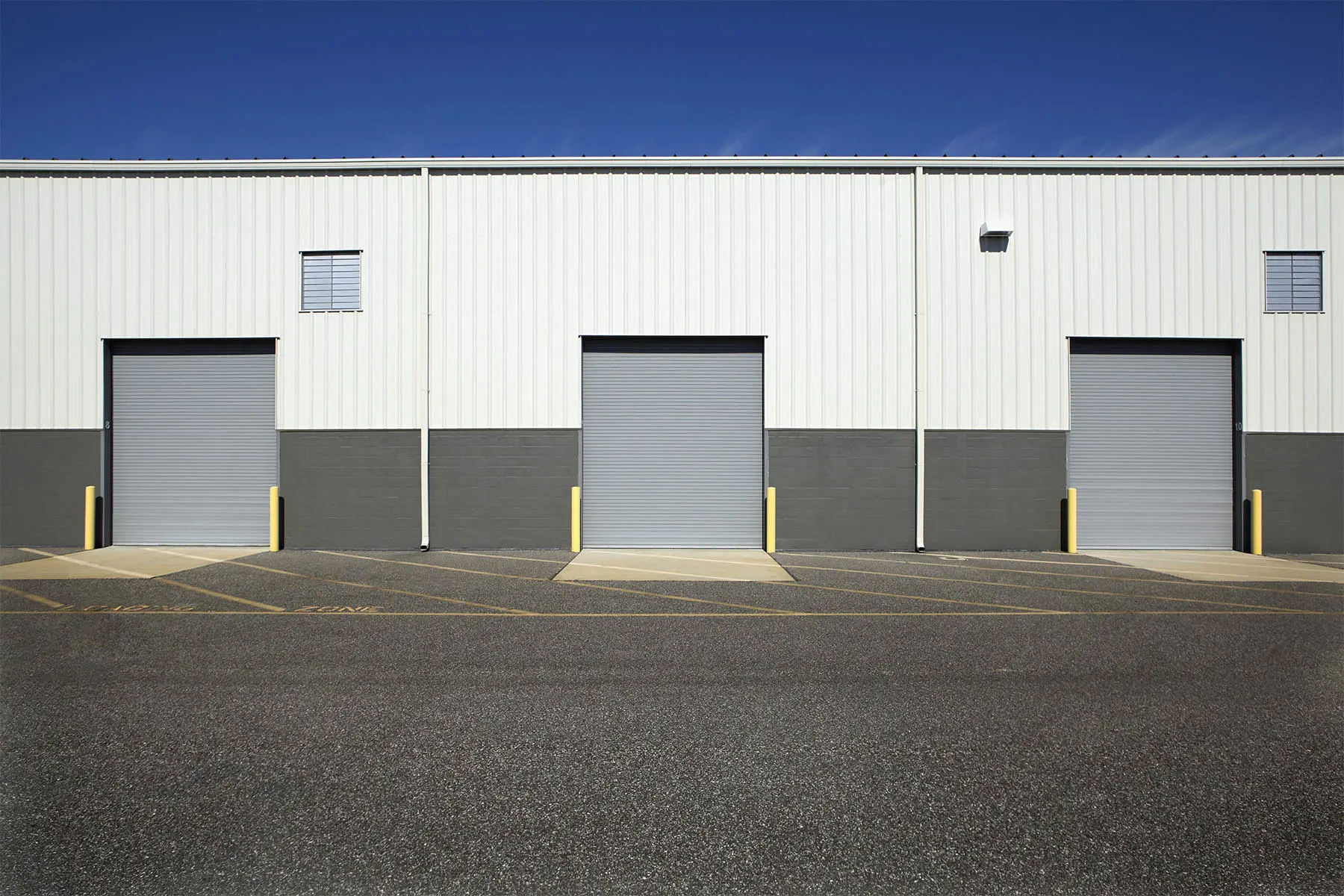 Warehouse facade with three roll-up loading doors and an empty paved yard