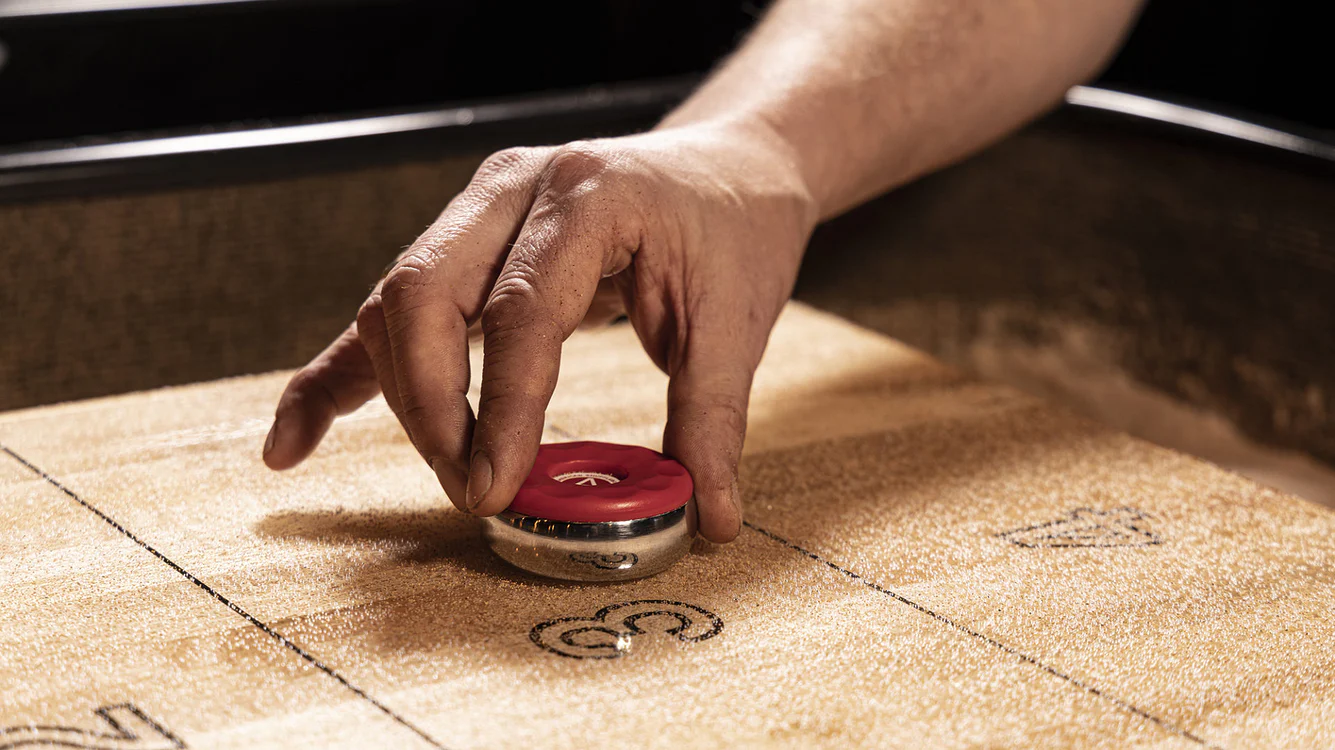 A young person with curly hair smiles at the camera while sitting in front of a laptop against a dark background.