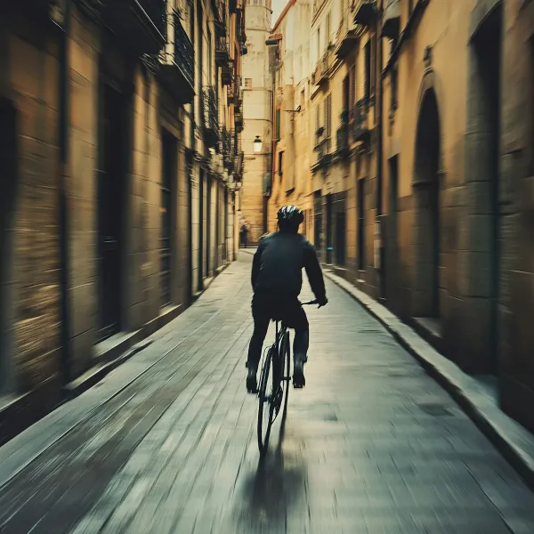 Vue de dos d'un cycliste circulant dans une rue pavée bordée de colonnes architecturales, illustrant la mobilité urbaine.