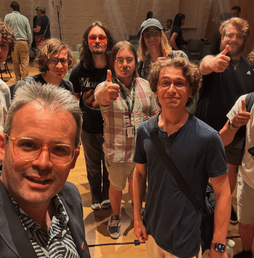 A man takes a selfie with young people smiling and giving a thumbs up