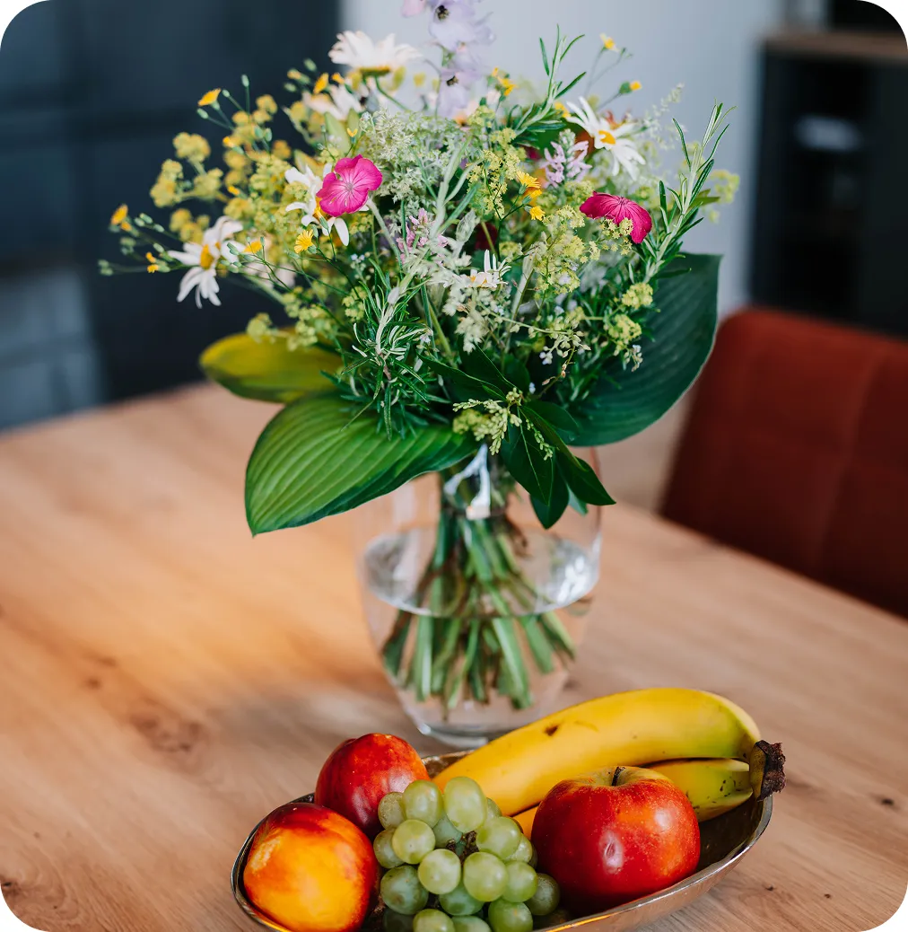 Blumenvase mit Blumenstrauß und Obstkorb auf dem Küchentisch.