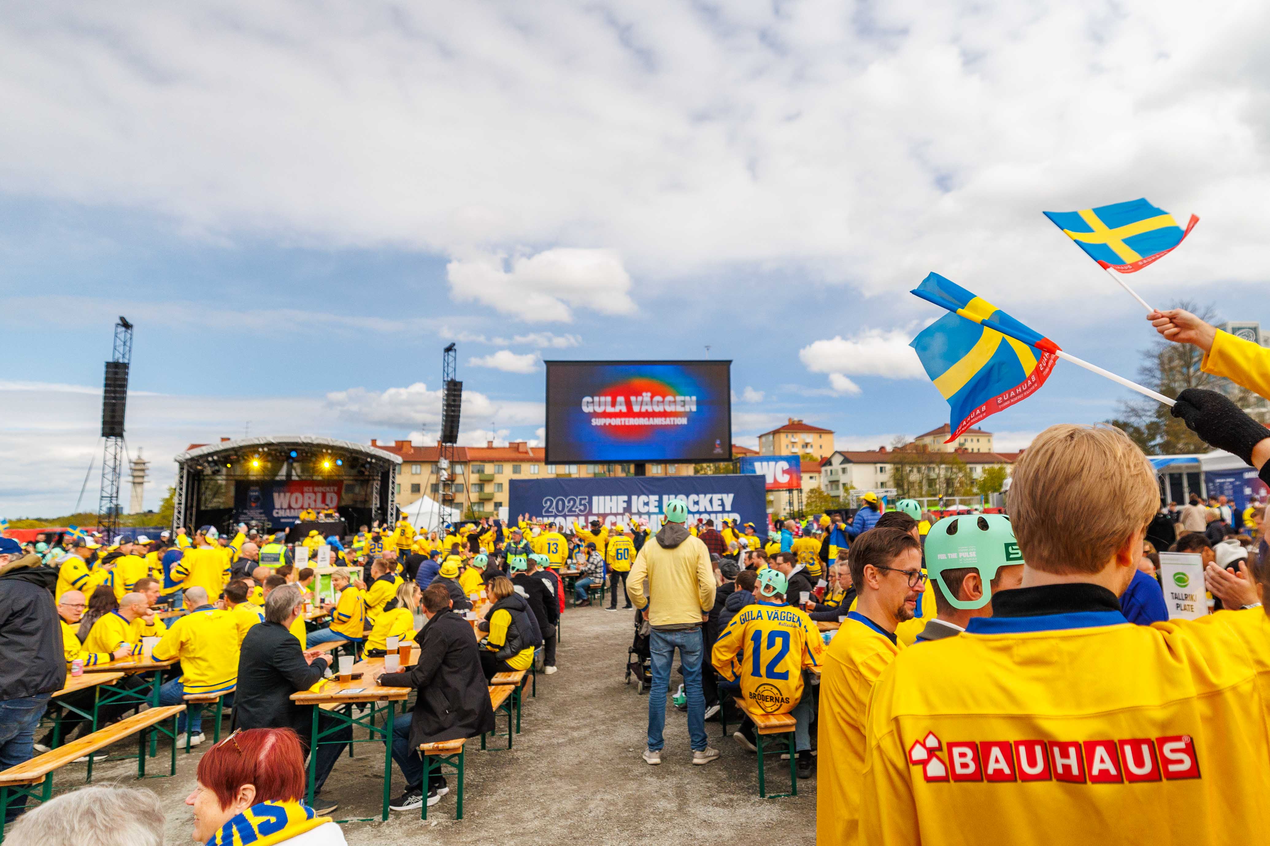 Enthusiastic Swedish hockey fans gather at the Gula väggen supporter zone in Stockholm, waving flags and enjoying the festivities of the 2025 IIHF Ice Hockey World Championship fan experience.