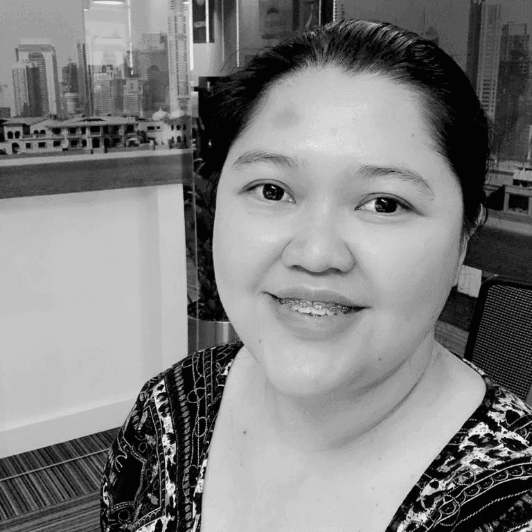 A woman seated at a desk in a minimalist workspace, reviewing architectural models. Large windows offer a view of a serene wooded area.