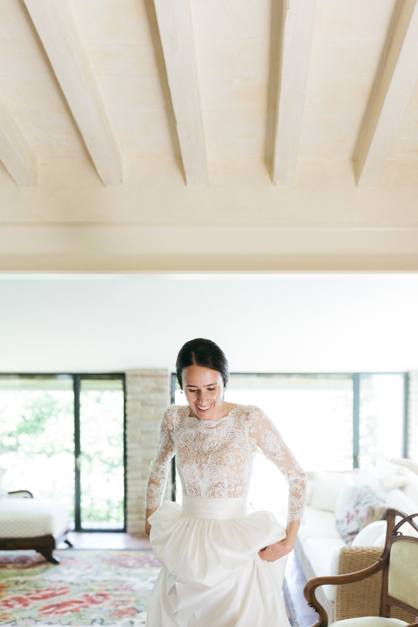 Sposa in abito bianco con pizzo trasparente e maniche lunghe nei preparativi matrimoniali, villa con soffitto in legno