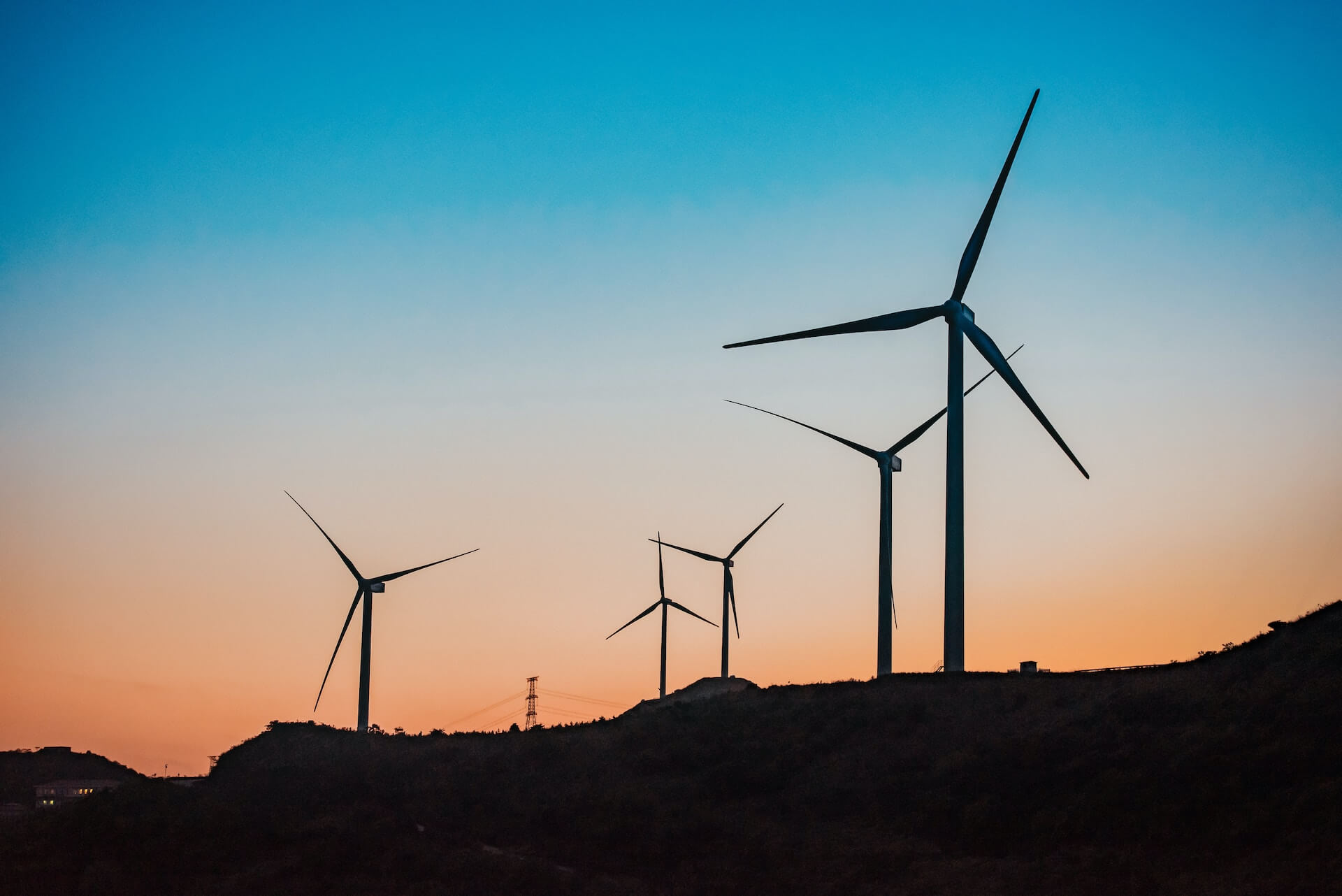 Wind turbines on mountains at sunset, harnessing renewable energy against a picturesque evening sky.