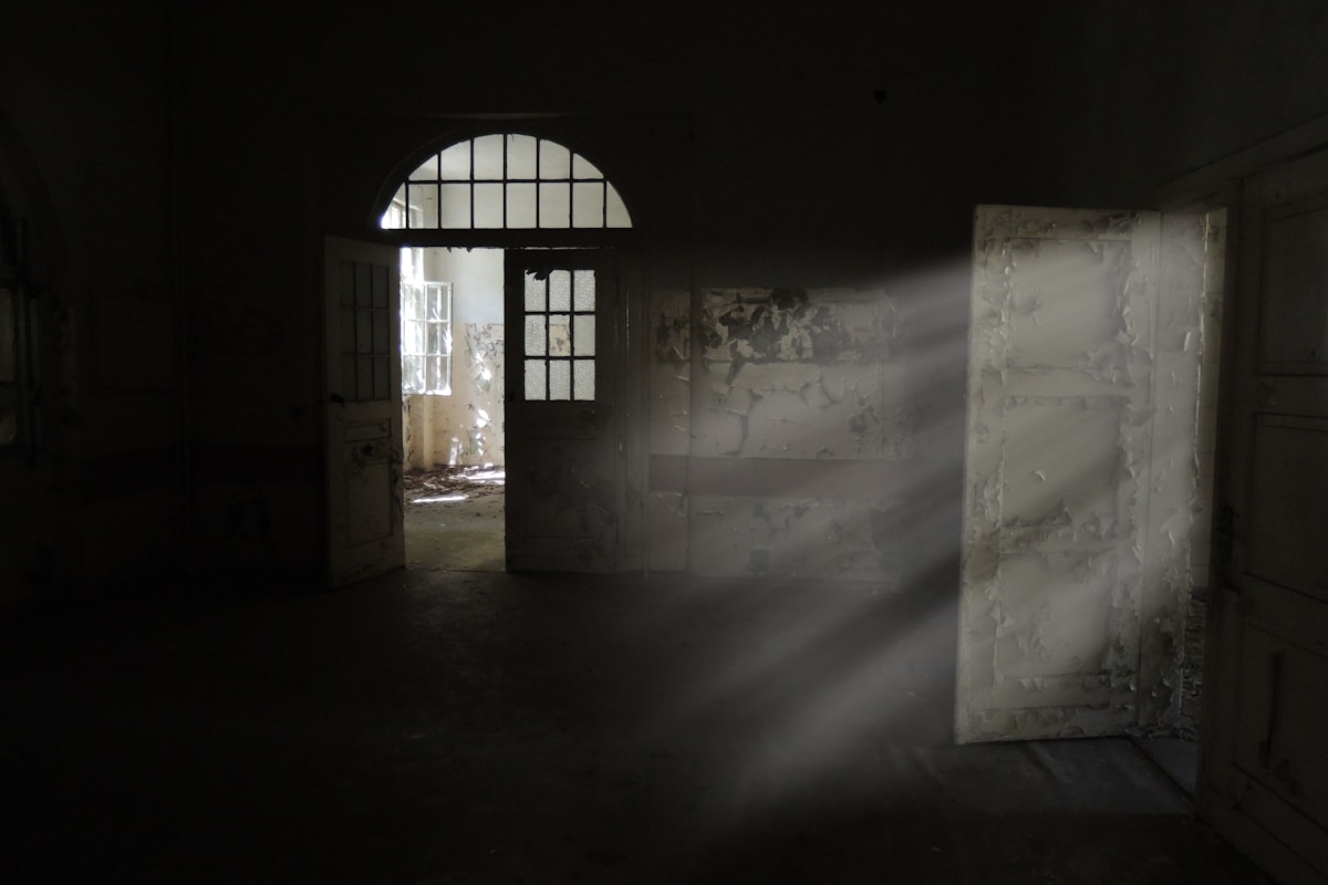 Dark derelict room with arched door and shafts of raking light