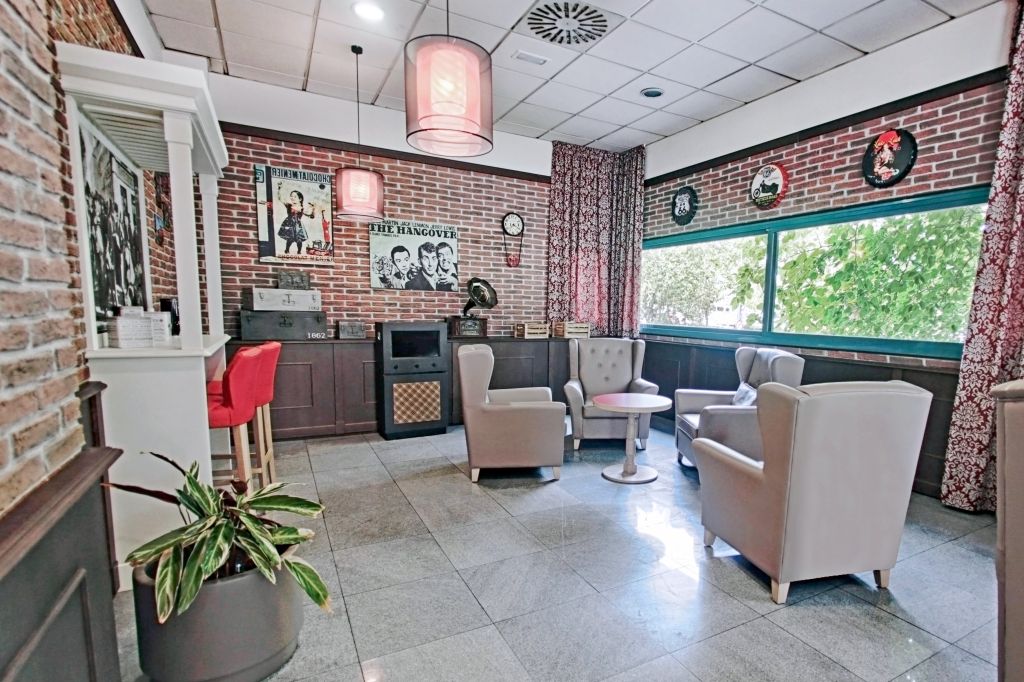Vintage-style lounge with brick walls, gray armchairs, movie posters, and pink pendant lights.