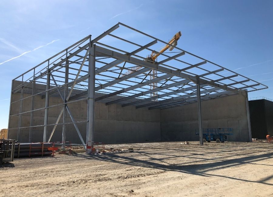 Structure métallique de bâtiment industriel en cours d’assemblage sur terrain dégagé.