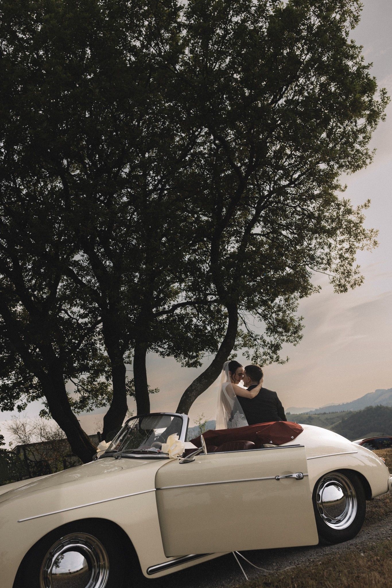 Sposi in convertibile vintage sotto il grande albero al Parco di Montebello, matrimonio in Emilia-Romagna