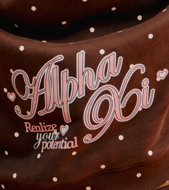 Close-up of a chocolate-brown Alpha Xi sweatshirt with pink lettering and white dot pattern.