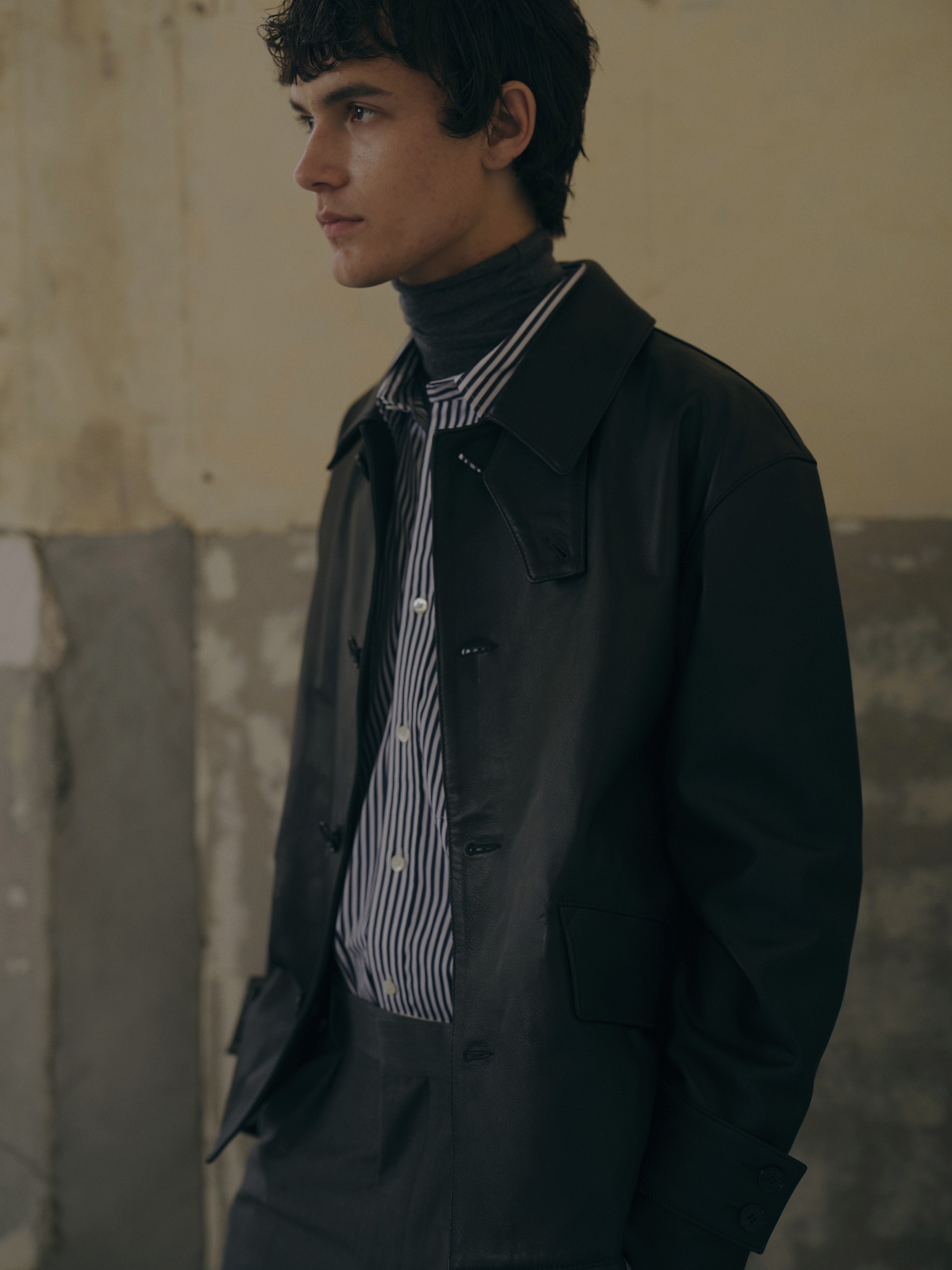 Plan américain d'un homme portant un imperméable marron, une chemise rayée et un col roulé