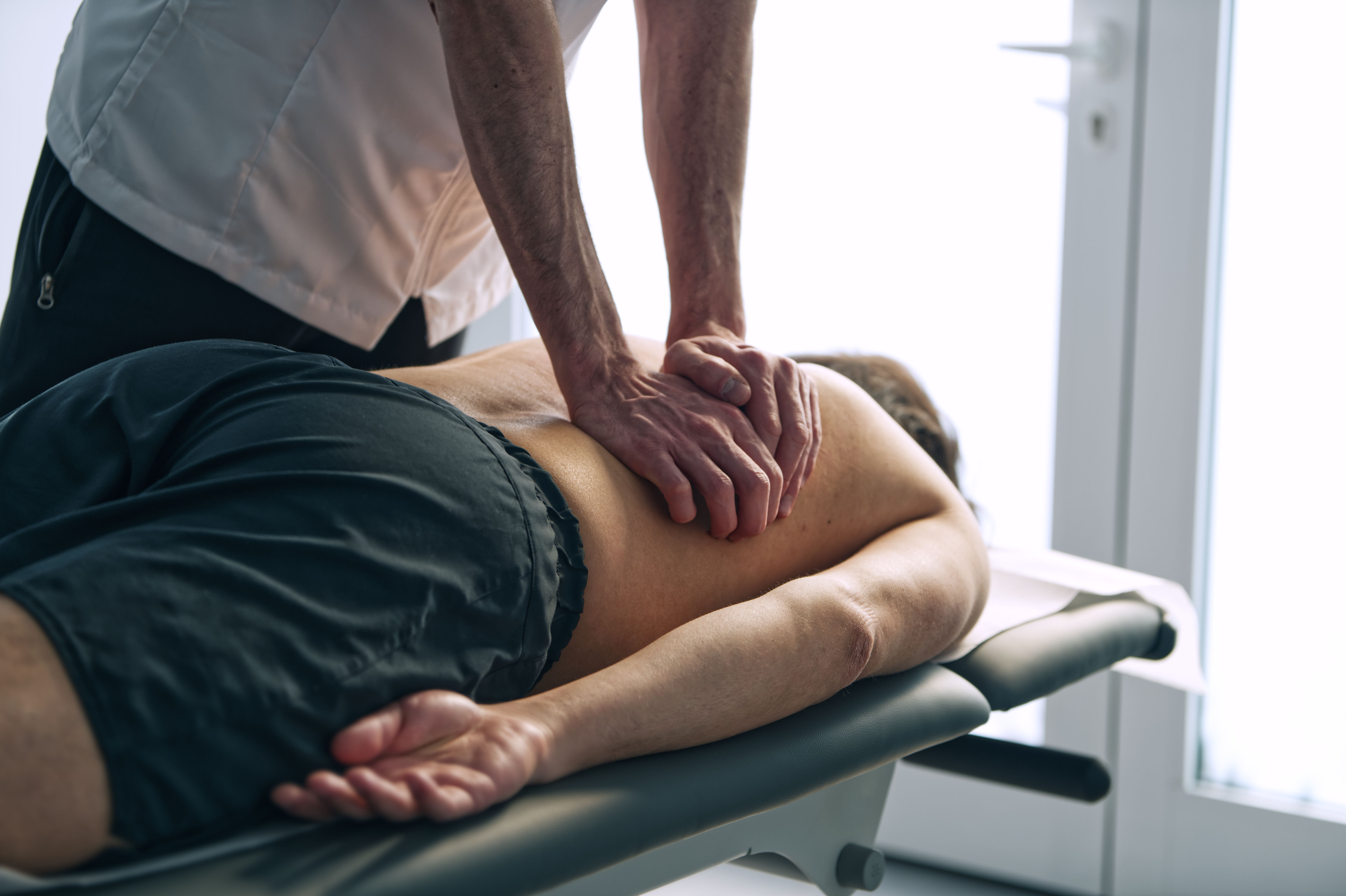 A person with glasses and a beard smiles warmly while working on a laptop at a desk. The setting is casual and relaxed, with a neutral background