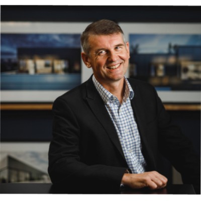 Smiling man in a suit with a blue tie, light brown hair, and a beard. Gray background, date at bottom: January 27, 2026. Professional, approachable.