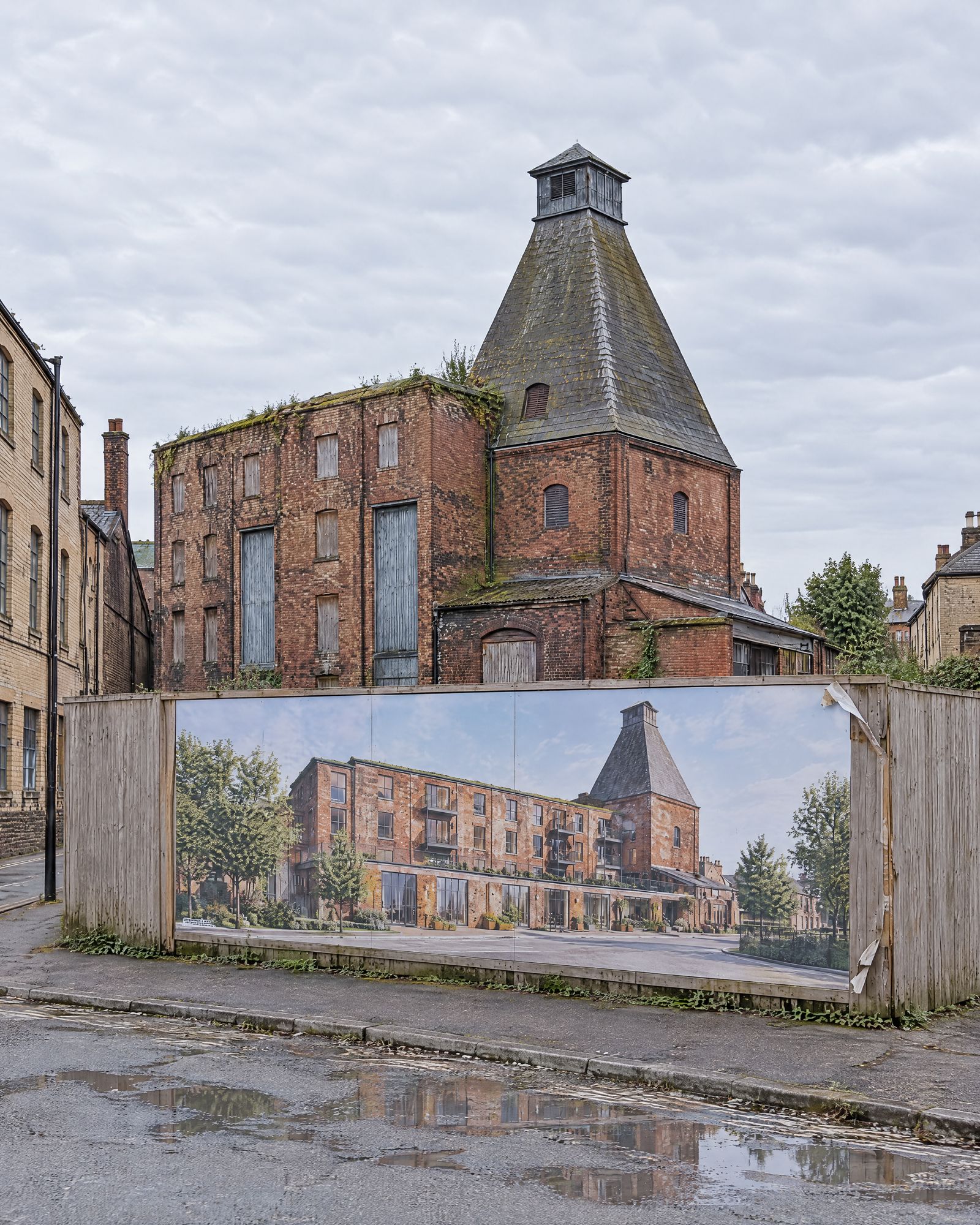 The maltings kiln rising above the timber hoarding that carries the printed render