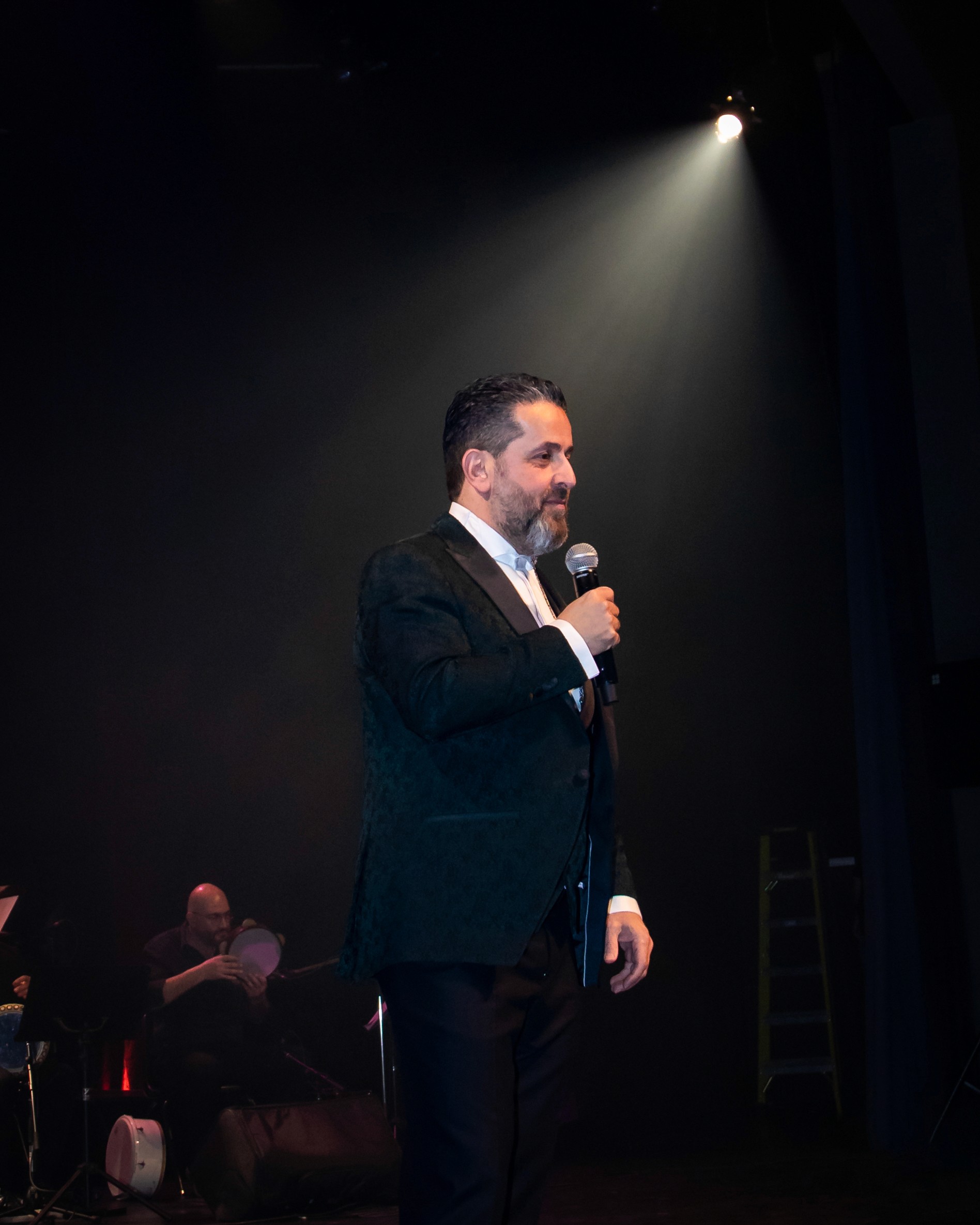 A woman with long dark hair wearing a black hijab, looking calmly at the camera against a muted background.