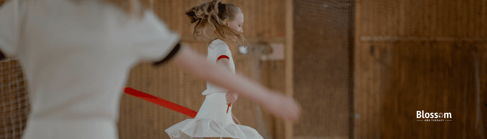 Two autistic gymnasts in white uniforms performing ribbon routines on gymnasium floor in Tennessee.