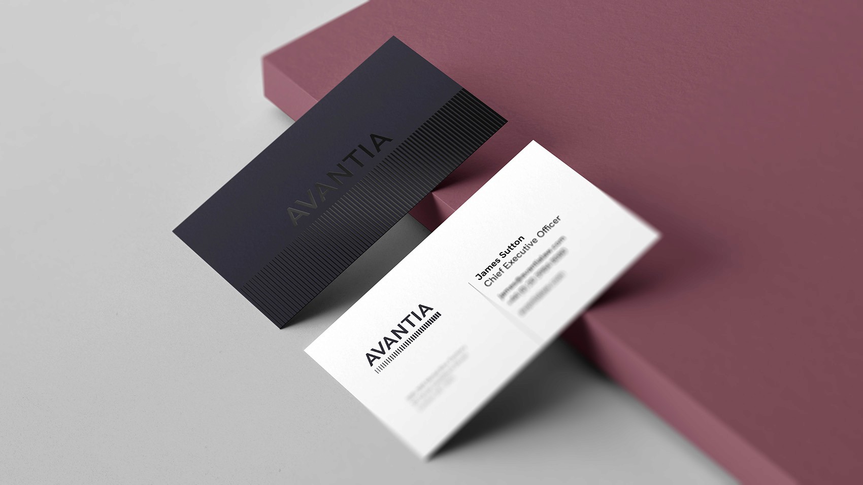 Two business cards displayed diagonally on a mauve surface. One is black with subtle vertical lines and the Avantia logo. The other is white with contact details for James Sutton, Chief Executive Officer, including phone number, email, and address.