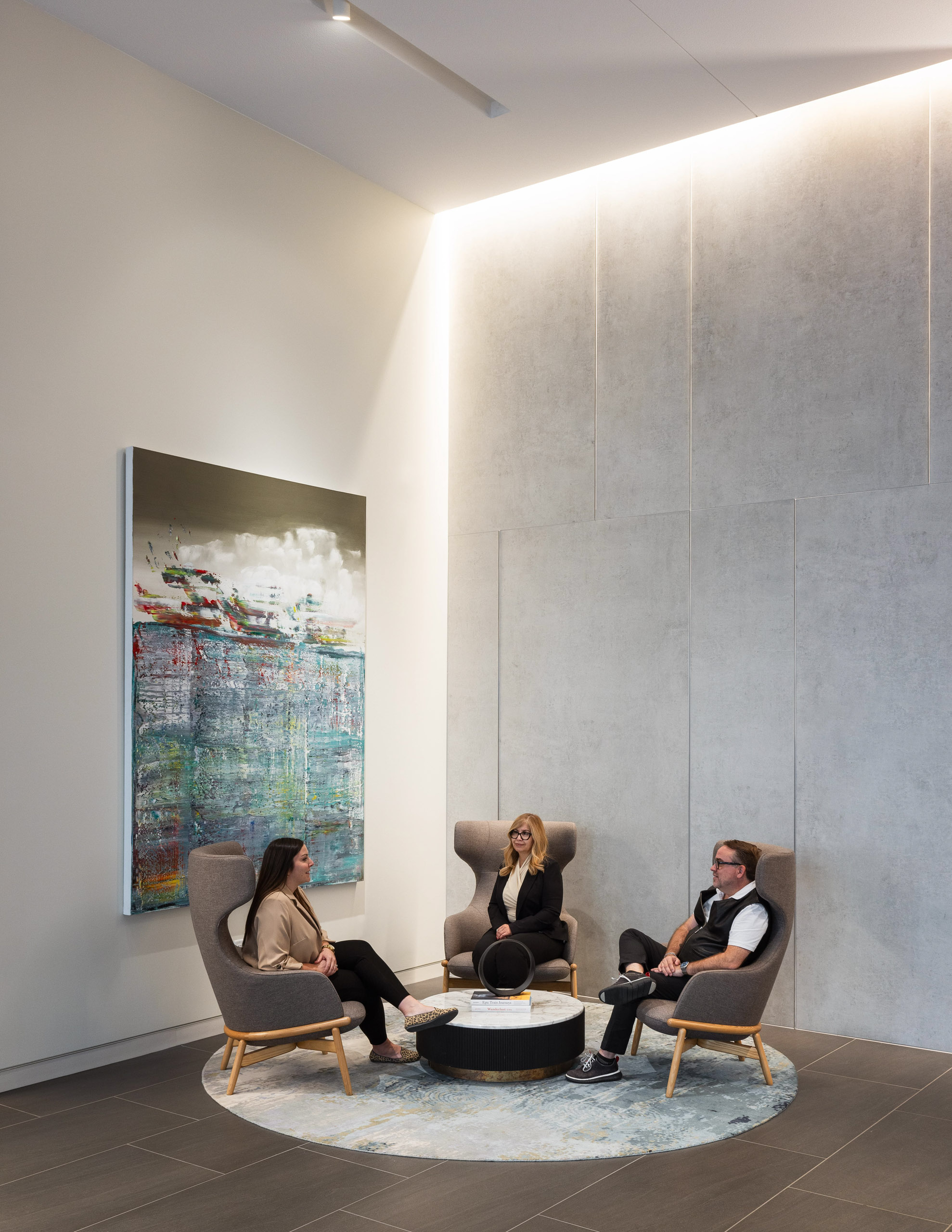 Three figures in repose on chairs around a coffee table.