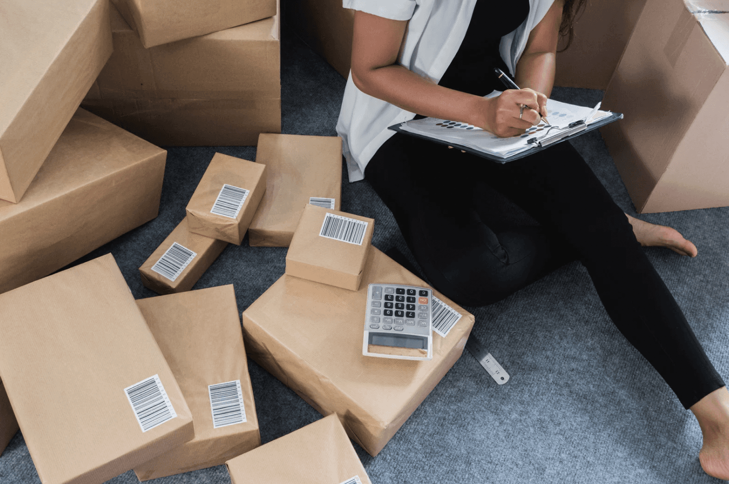 Seller surrounded by packages while taking inventory notes, illustrating the operational demands of scaling Amazon businesses during high-volume periods.