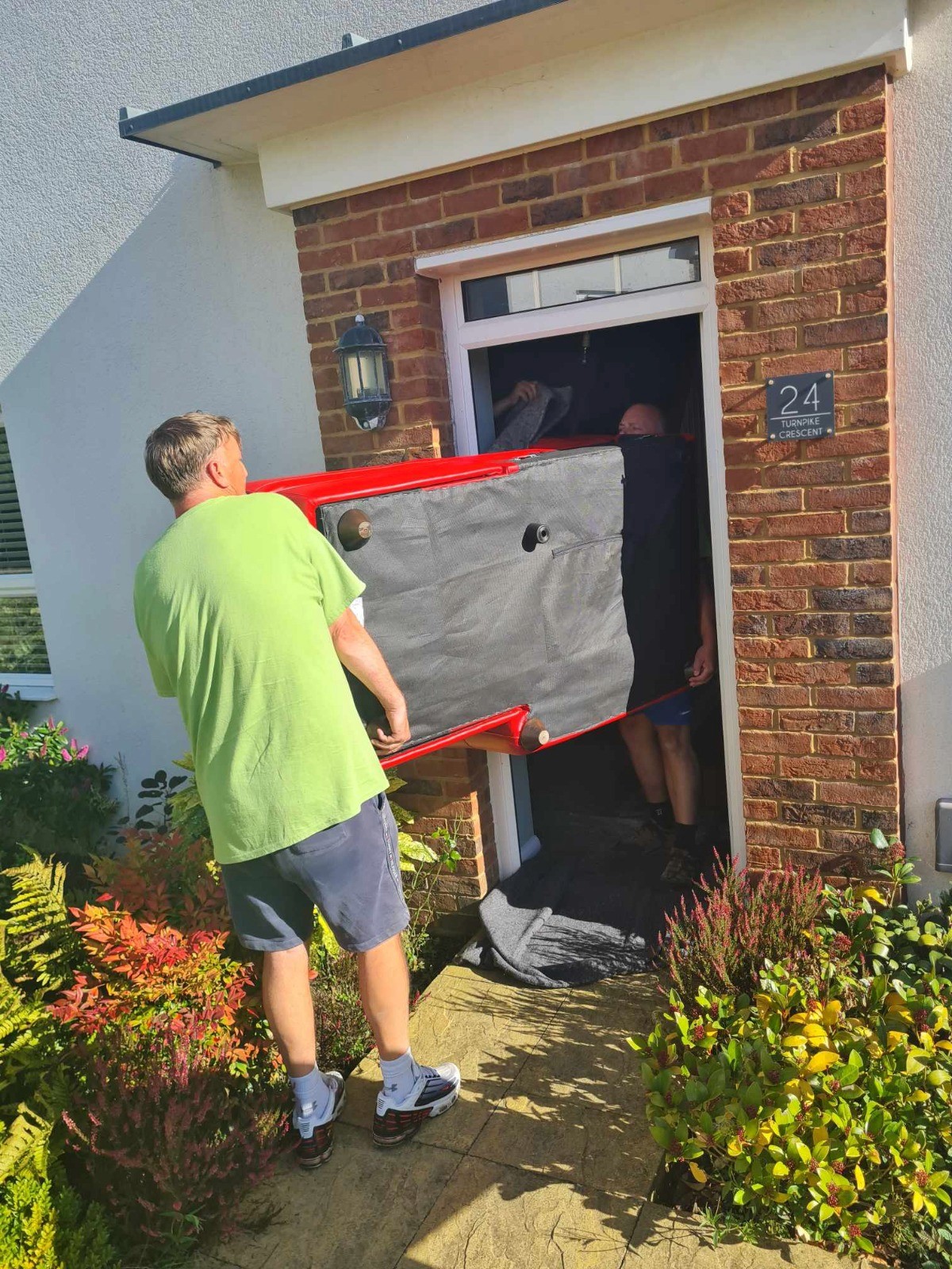 Moving On Removals staff in lime green uniforms safely navigating a narrow doorway while moving furniture with protective padding.