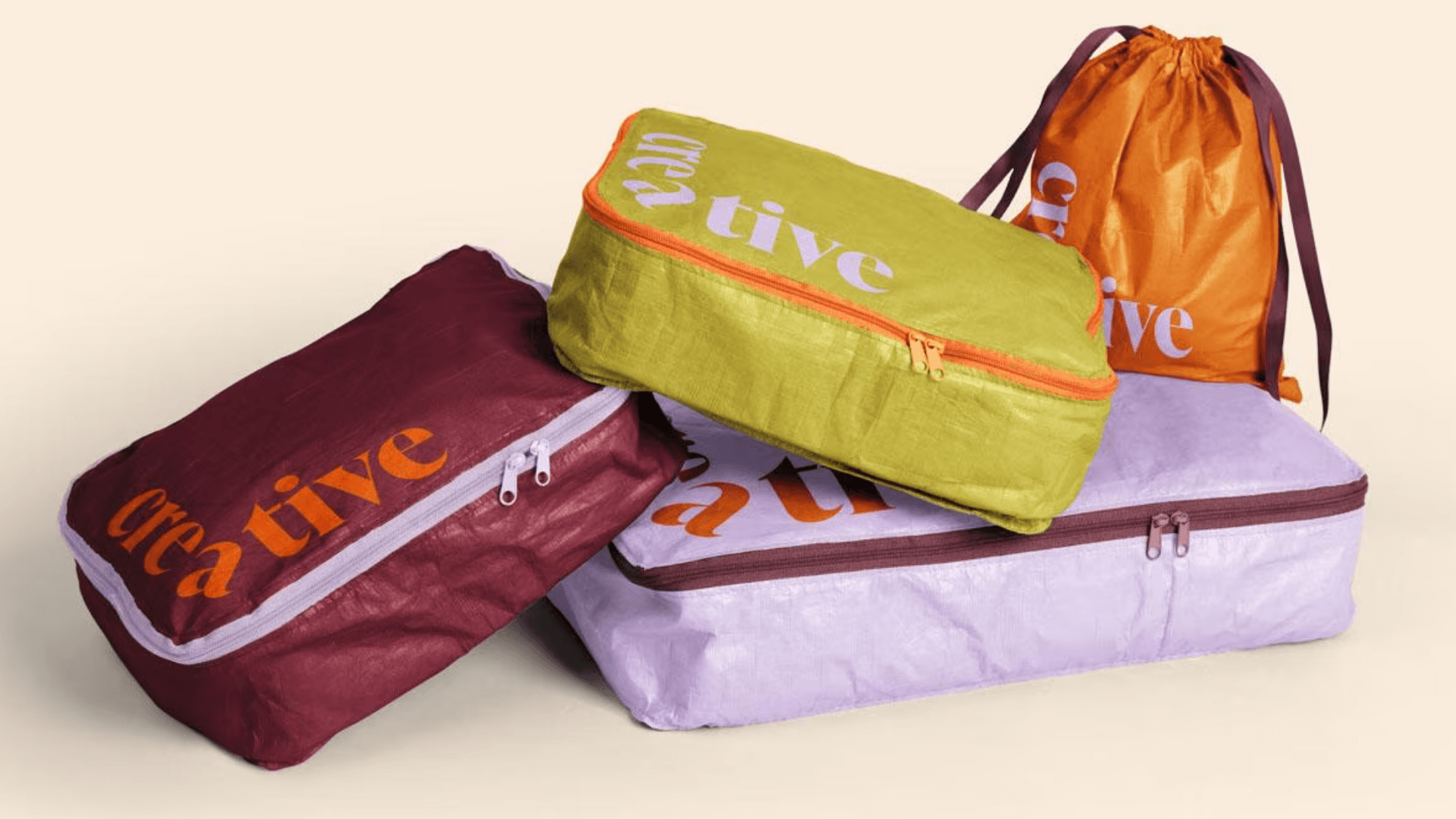 Three packing cubes and a drawstring that are branded and are all different colors on a tan background.