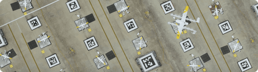Overhead view of a drone delivery nest, displaying several Wing drones parked on designated squares with distinct white alphanumeric codes, showcasing organization and airplane storage.