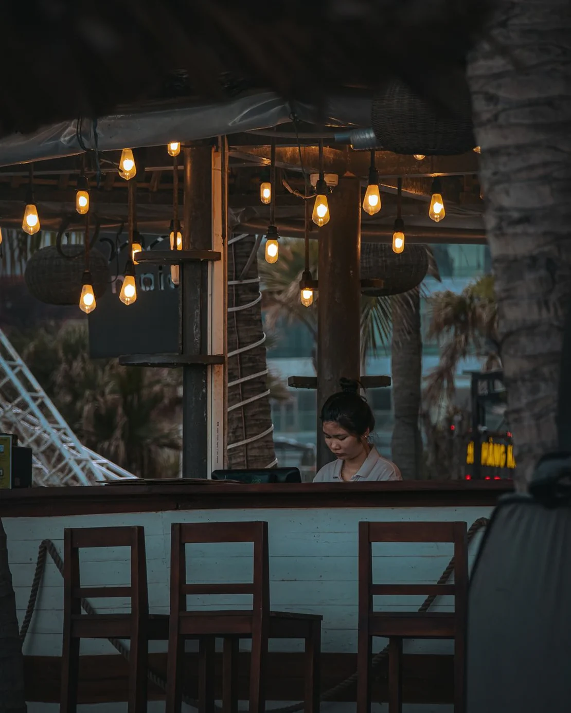Staff member working inside a beachfront restaurant with warm hanging lights.