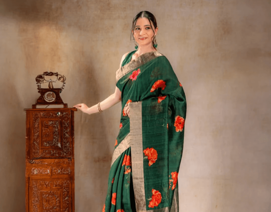 A woman wearing a green Dupion silk saree from That Saree Shop, featuring elegant golden borders and delicate orange floral prints, blending textured luxury with vibrant handcrafted detail.
