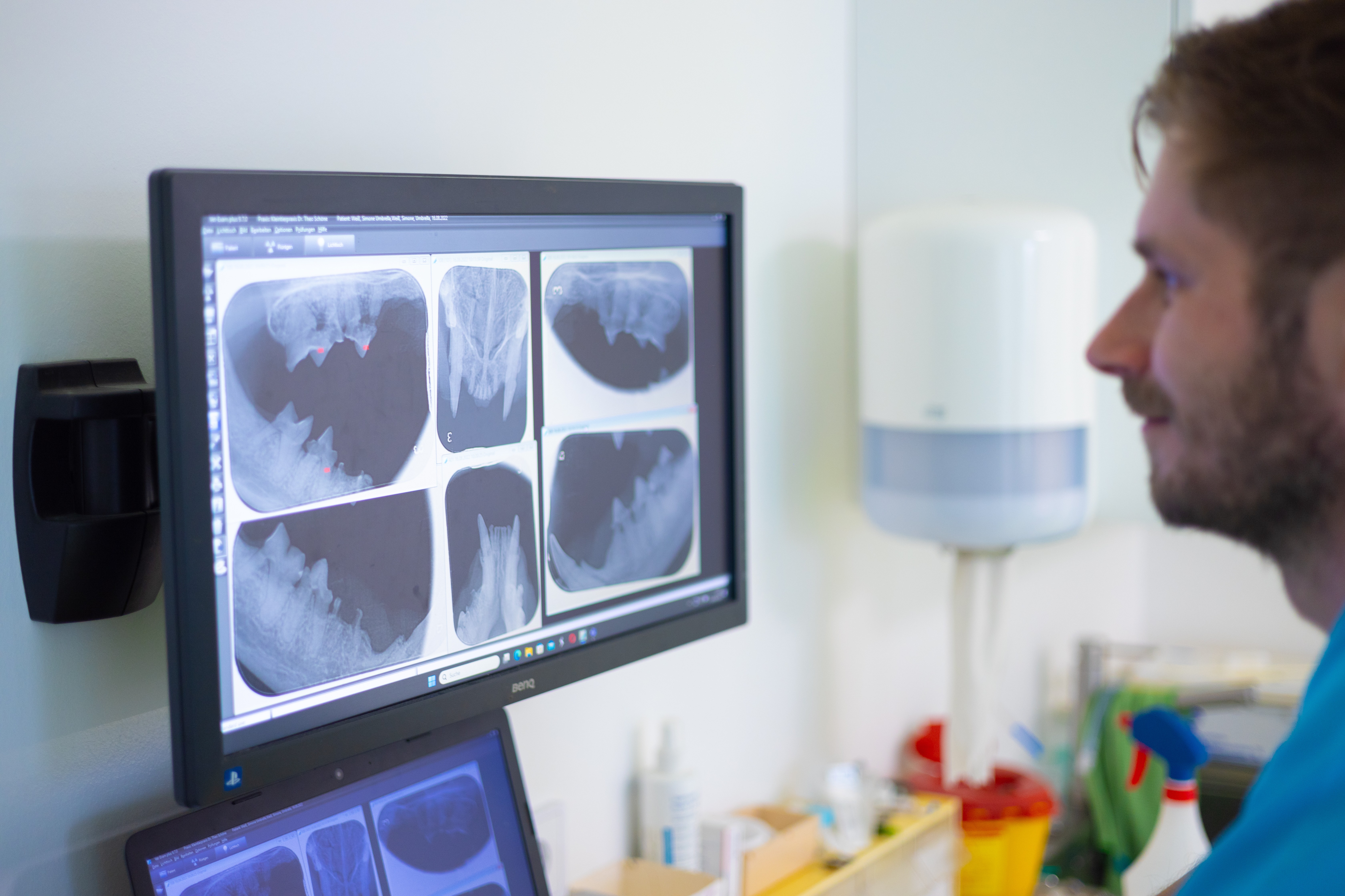 Ein Tierarzt in Tierarztpraxis betrachtet Röntgenaufnahmen. Der Arzt trägt blaue Kleidung und hat einen Bart.