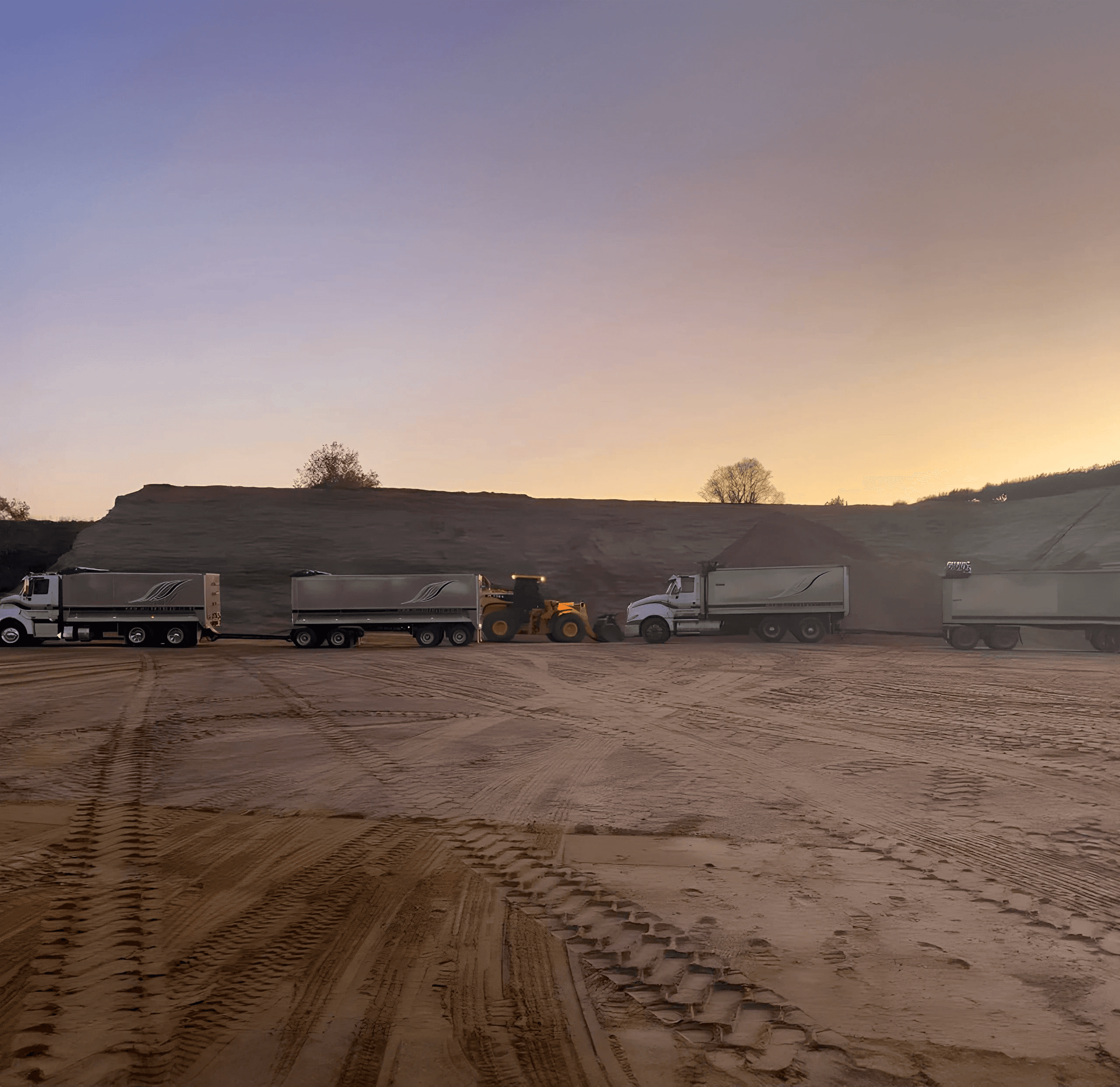 Two trucks and loader in a sand quarry at sun rise