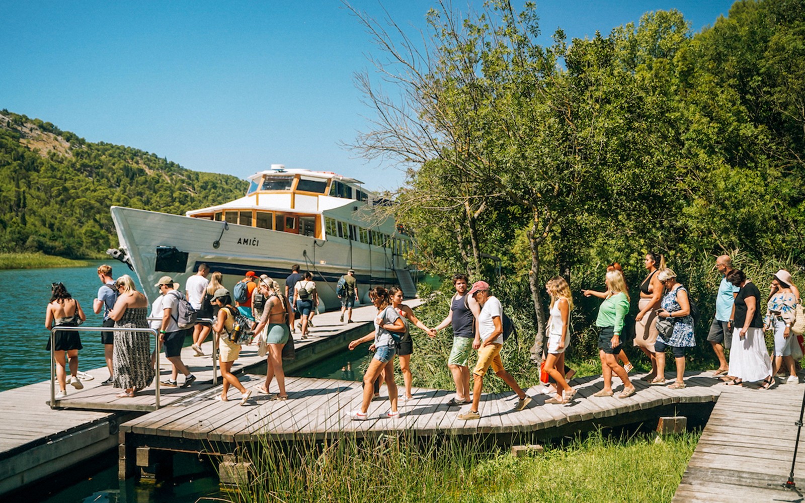 Turistas caminando por un sendero de madera cerca de un barco en el Parque Nacional de Krka.