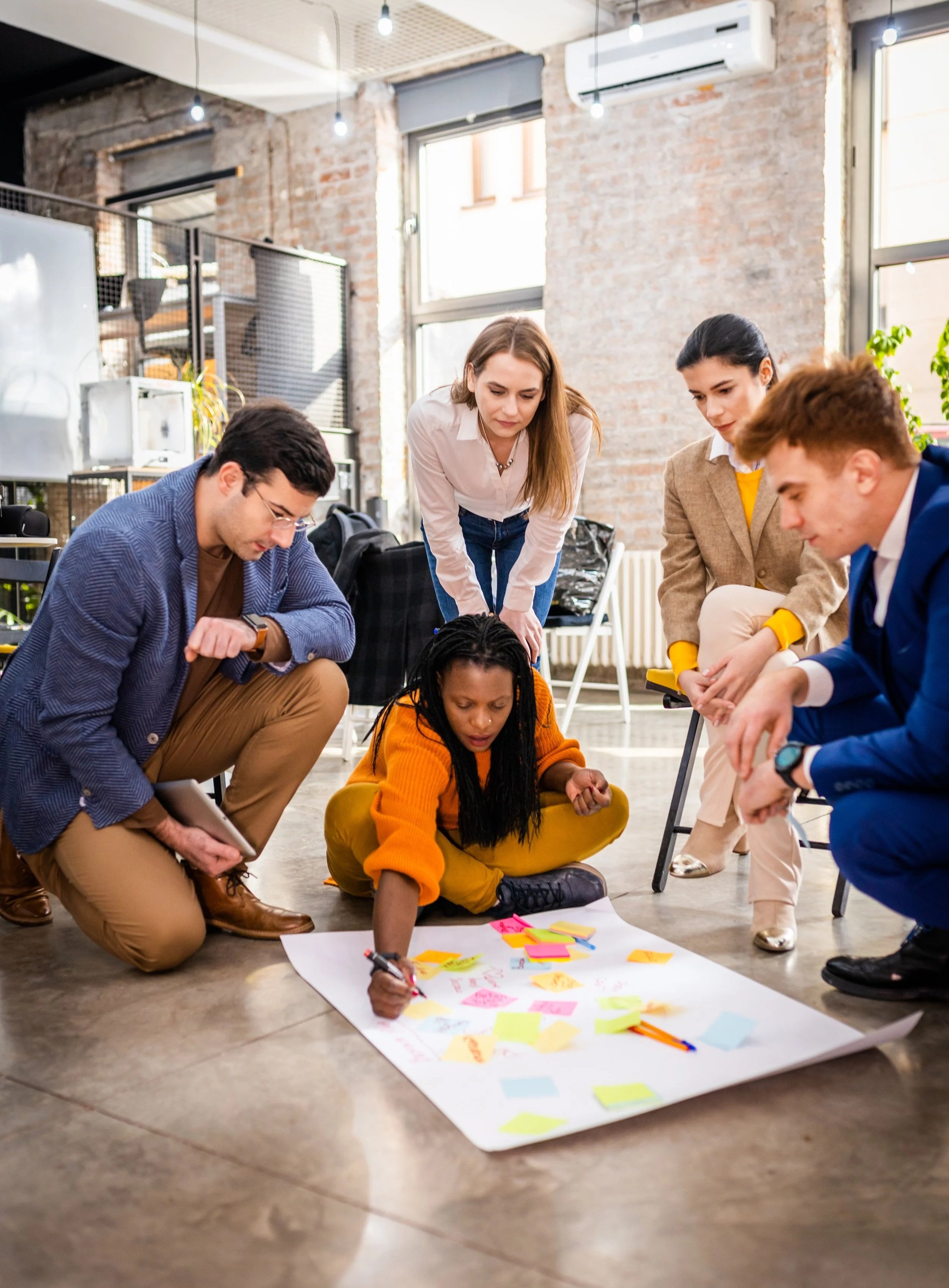 A group gathered around a large planning sheet and sticky notes on an office floor.