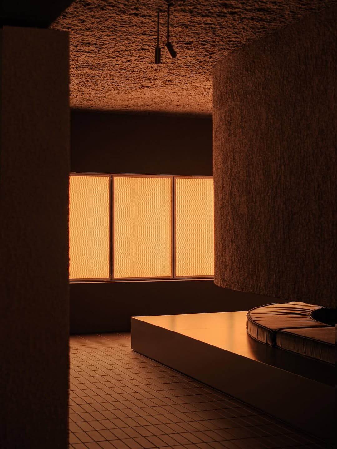 Warm geometric interior with a low platform, tiled floor, textured walls, and a round cushion.
