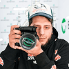 Man in hoodie and hat holding camera.