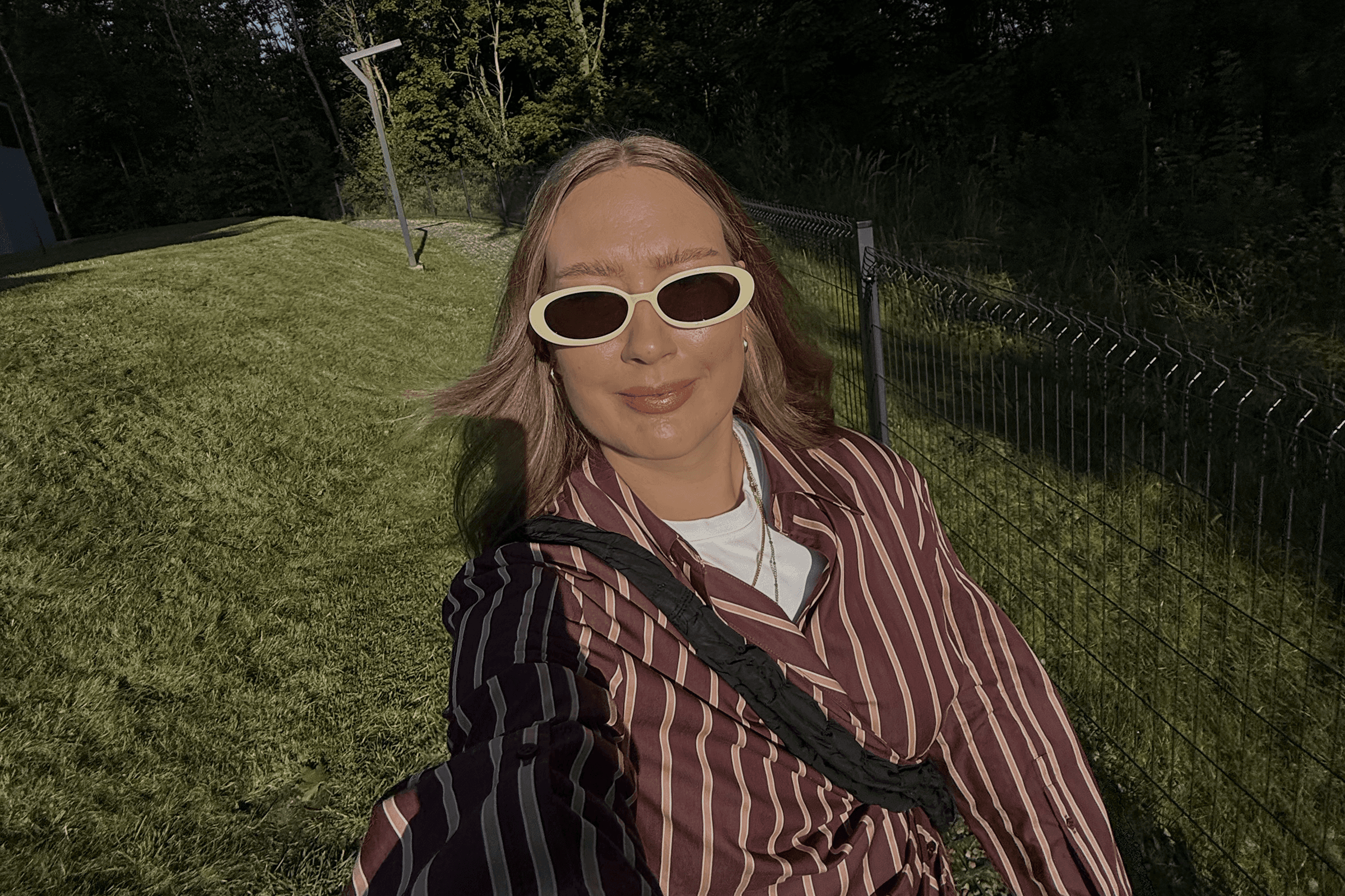 Smiling Joanna Cieszyńska wearing sunglasses and a striped shirt. In the background there's grass.