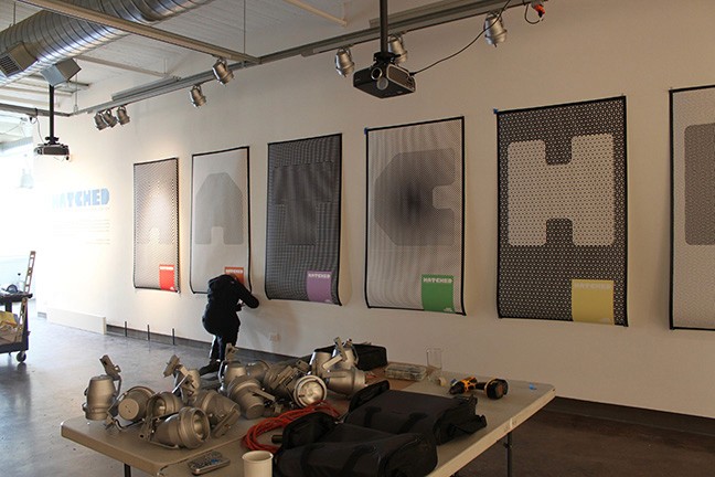A set of black and white printed posters that show a letter and a colorful square near a corner with text Hatched.