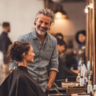 Hairdresser works diligently on a customer's hairstyle in a stylish salon, with mirrors and hair products in the background.