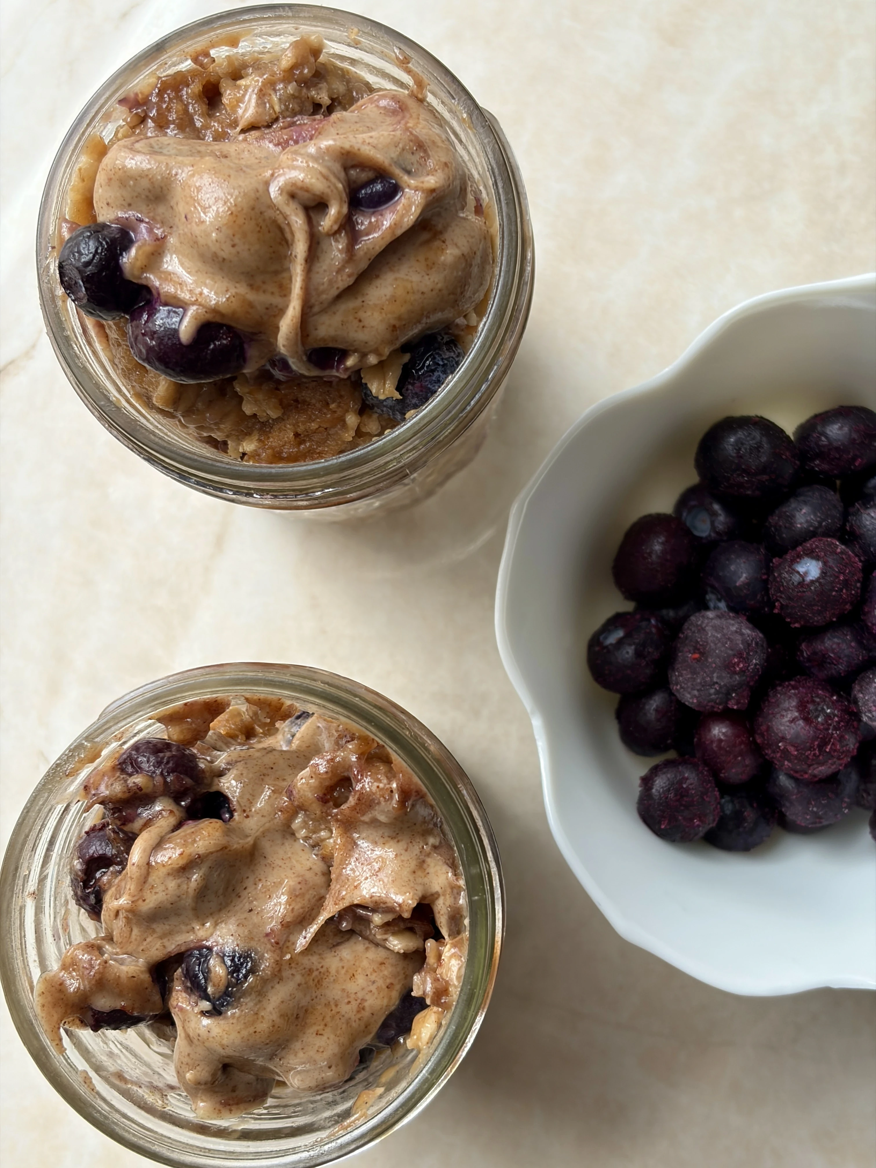 high-protein blueberry muffin overnight oats in glass jars with almond butter on top and a side of fresh blueberries