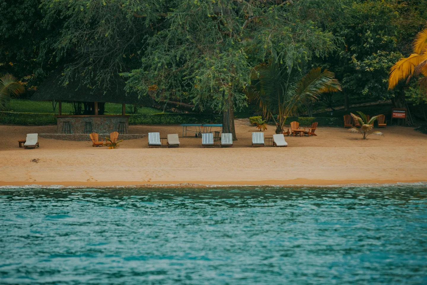 Quiet sandy beach with lounge chairs beside calm ocean water.