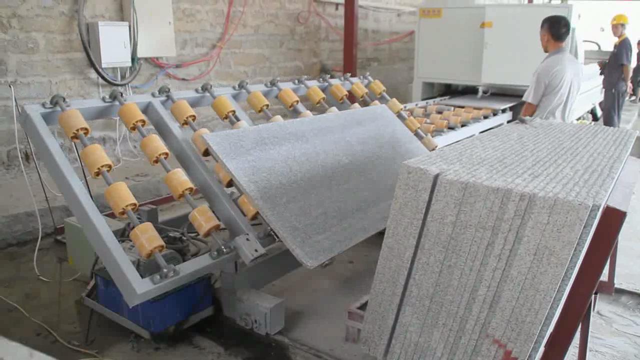 A stone slab being processed on a conveyor system in a stone workshop, showing precise positioning with yellow rubber rollers.