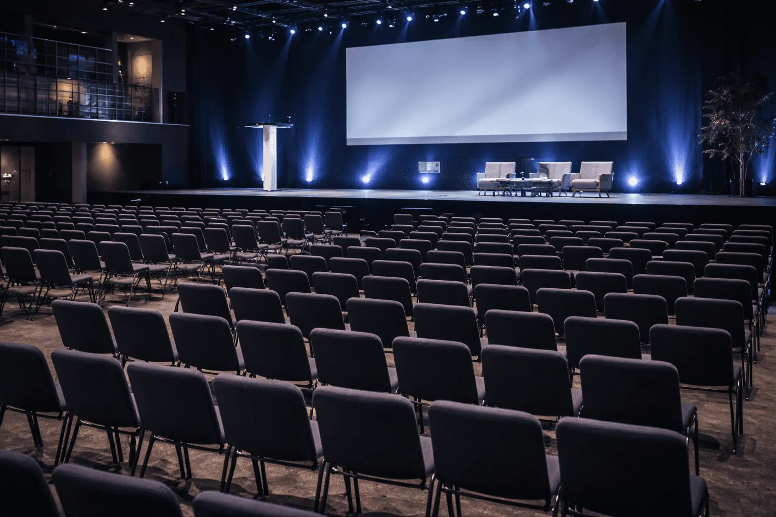Empty auditorium with rows of chairs and a large stage screen.