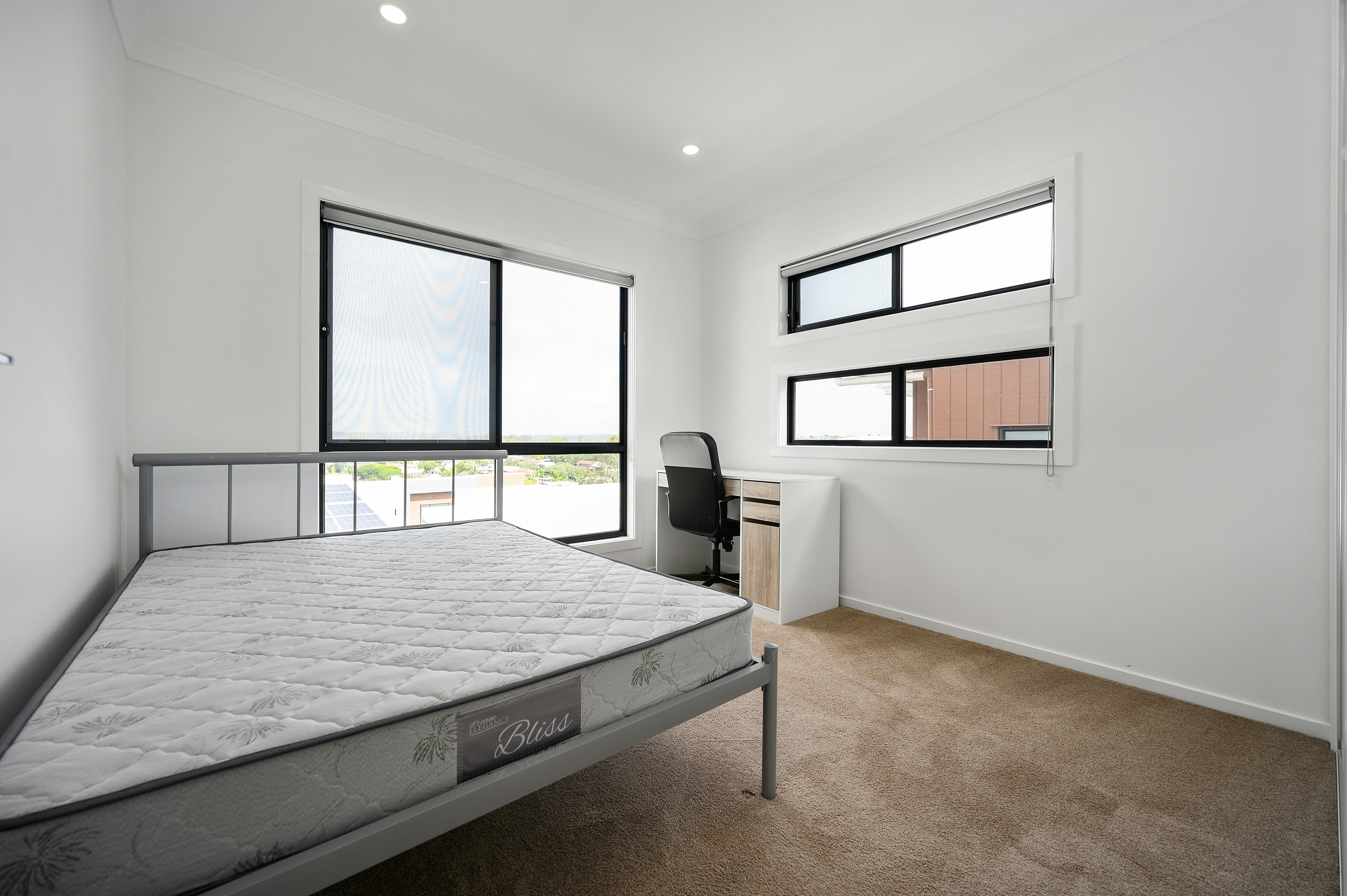 White wall bedroom with a mattress on the bedframe and two windows