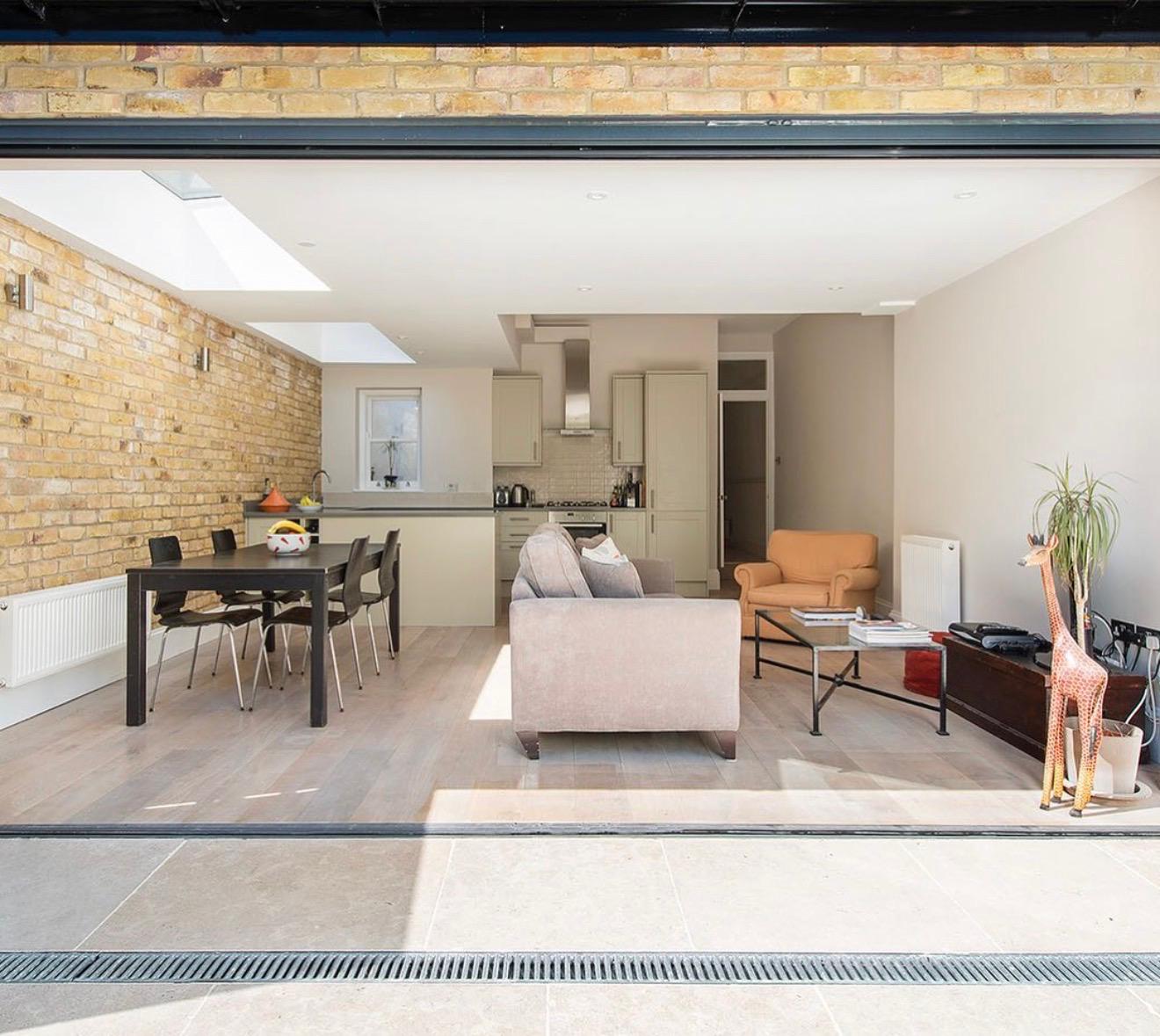 A serene outdoor seating area with two chairs, surrounded by lush greenery and a glassed-in structure.
