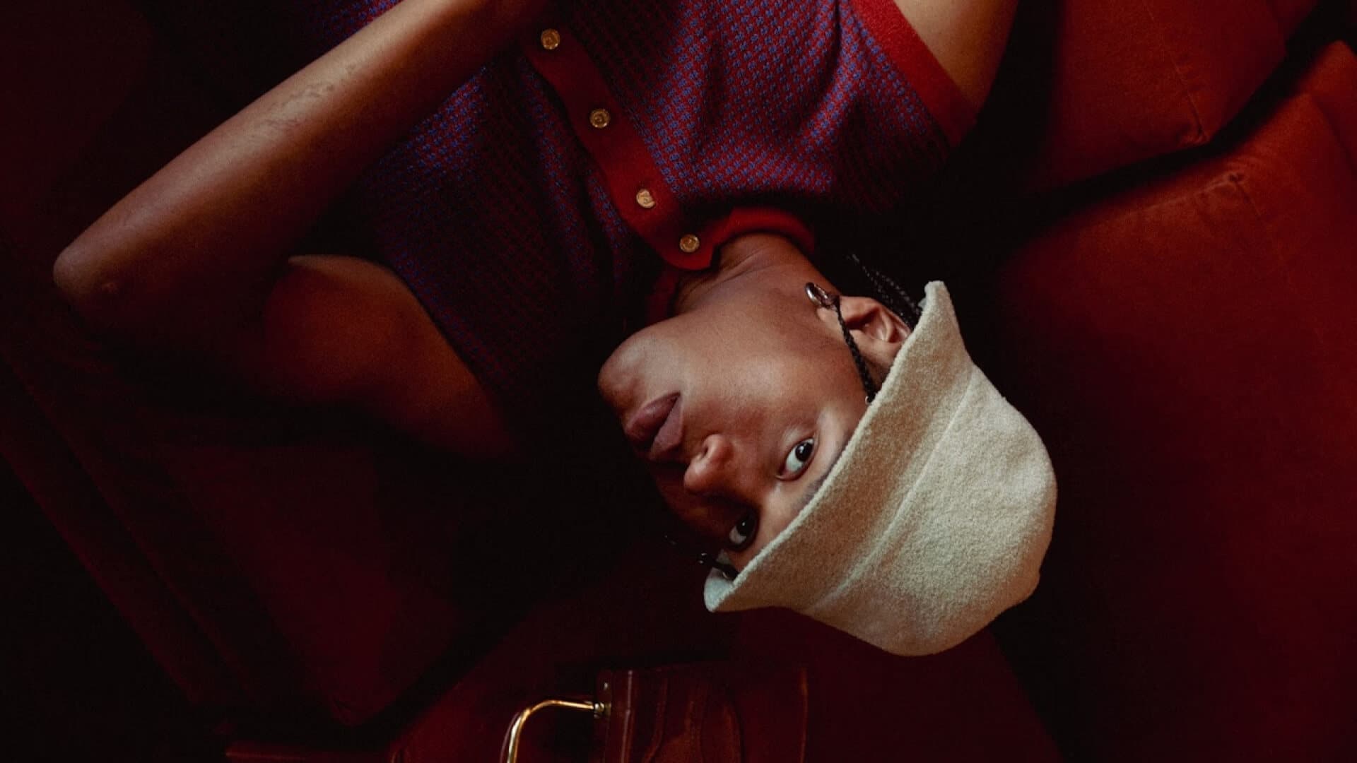 Fashion model reclining on a red sofa in a styled interior setting, cinematic lighting and art direction – professional film production logistics and on-set coordination.