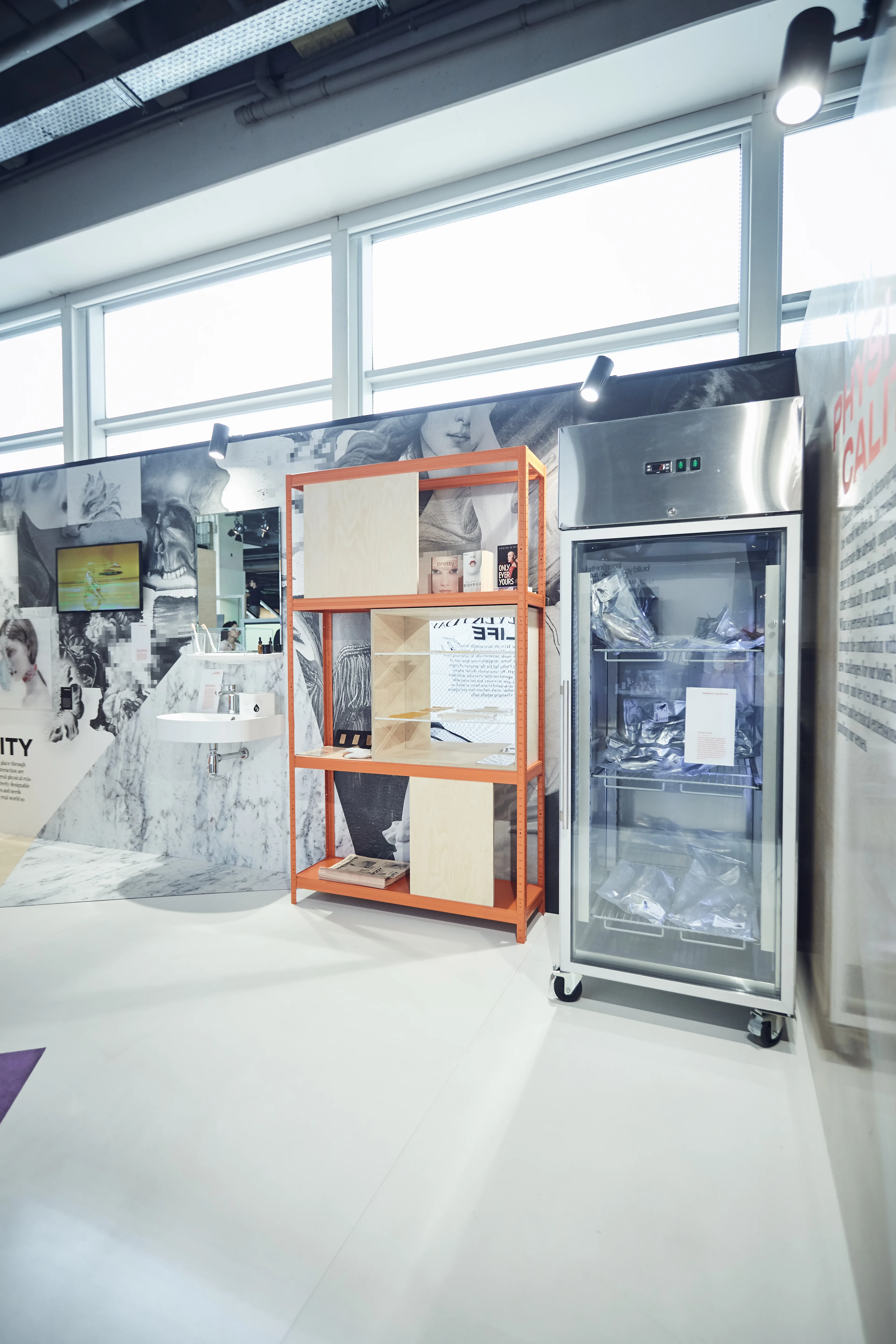 Orange shelving unit and a stainless-steel display fridge in front of collage walls at the Cosnova Future of Body and Beauty exhibition.