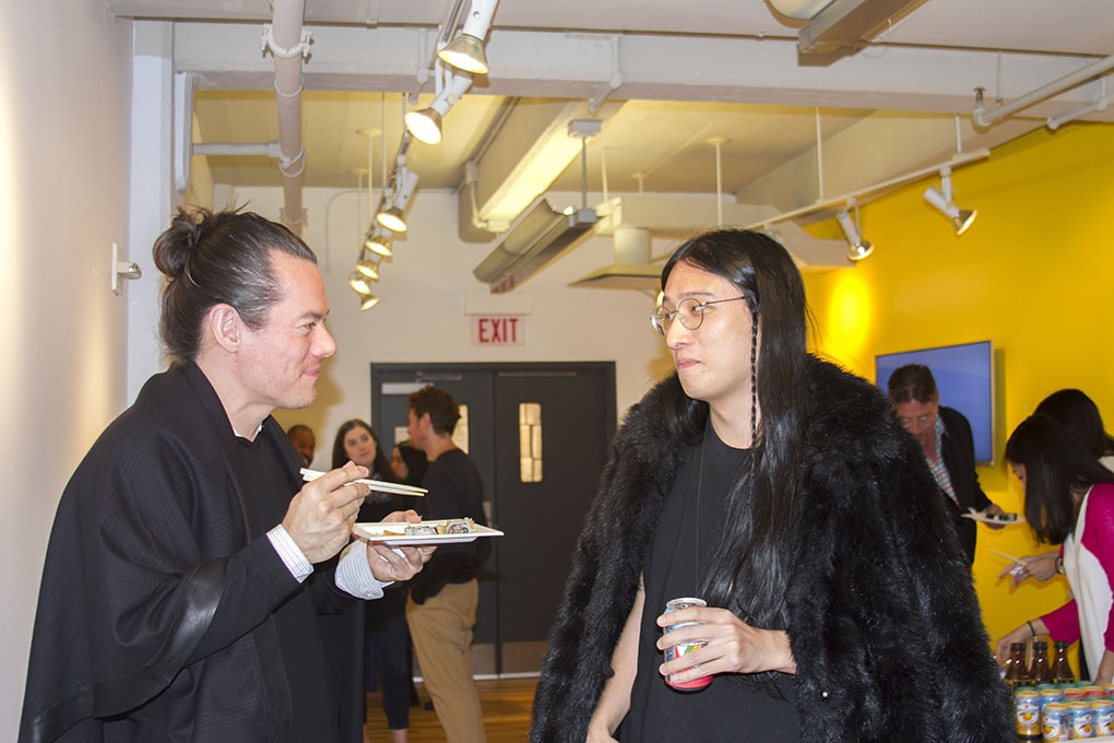 A photo of two people sitting in an exhibition room, while having a snack or drinking a soda.