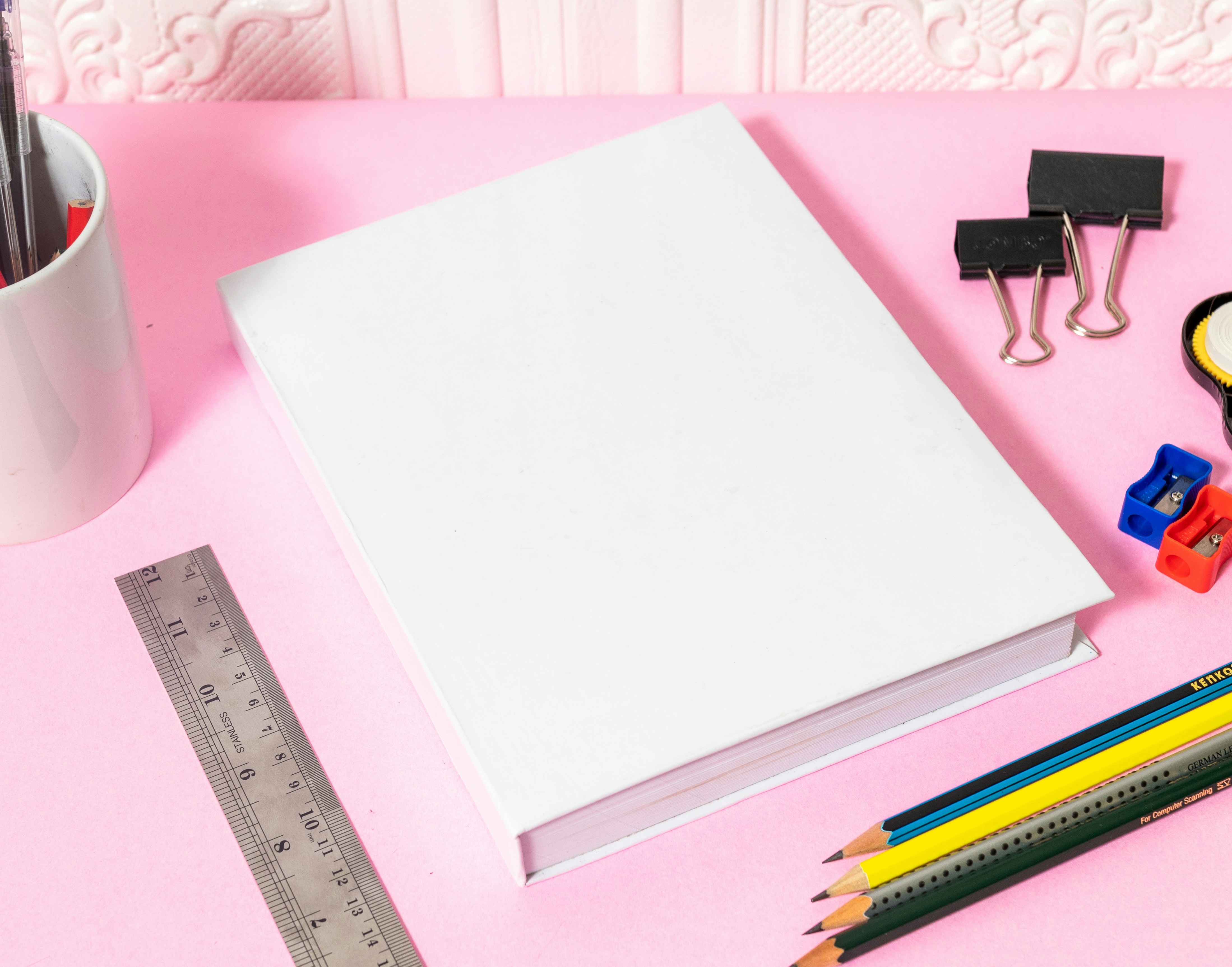 a notebook, pencils, ruler, tape, and pencils on a pink